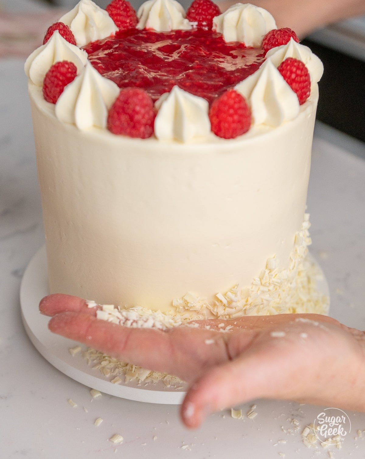 hand pressing white chocolate shavings onto the side of the cake