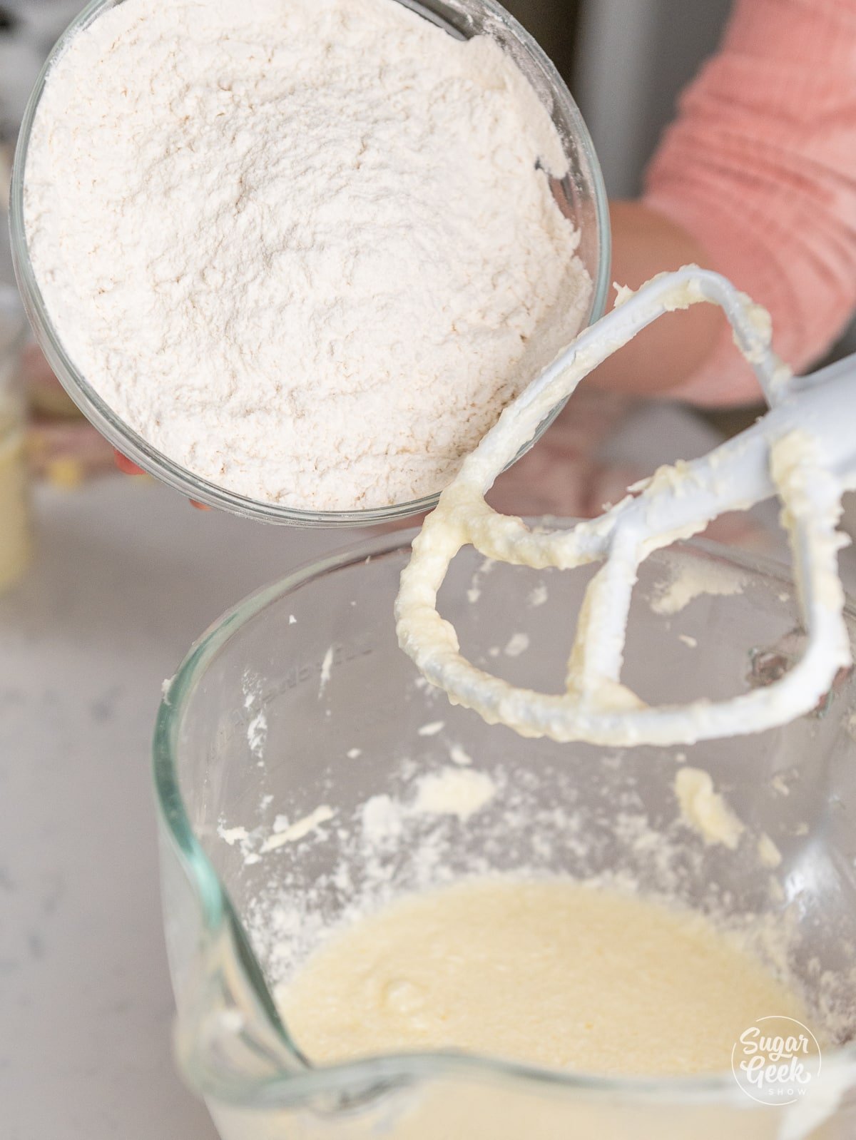 bowl of flour pouring into a glass stand mixer bowl