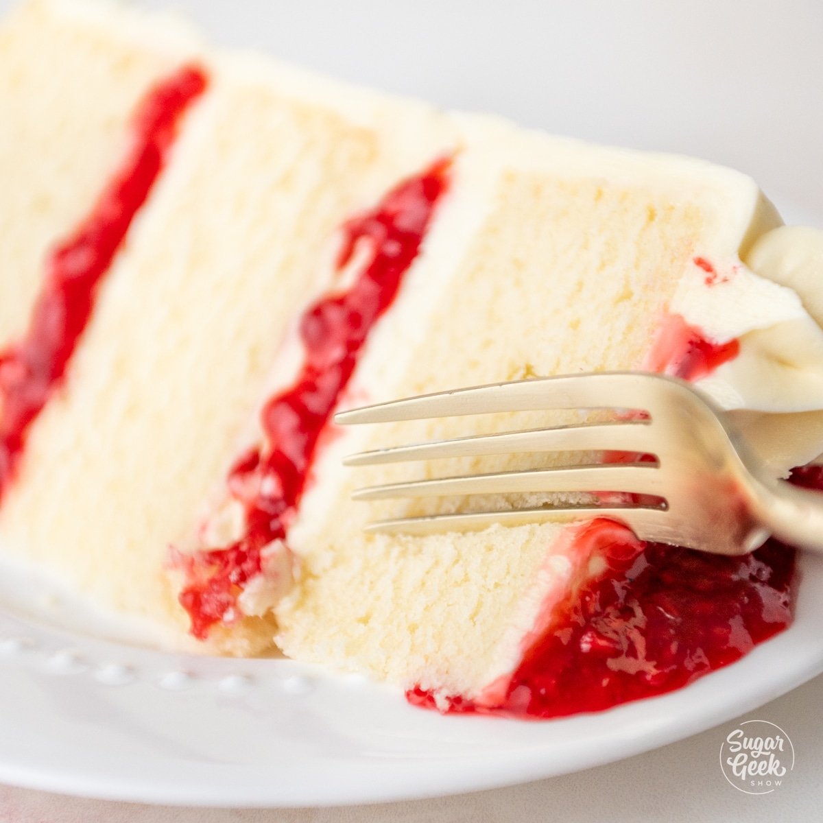 fork slicing into a piece of white chocolate raspberry cake