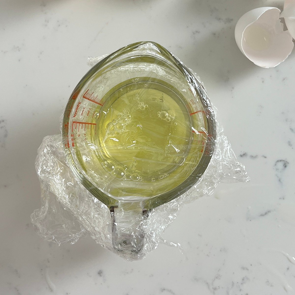 plastic wrap covering egg whites in a measuring cup