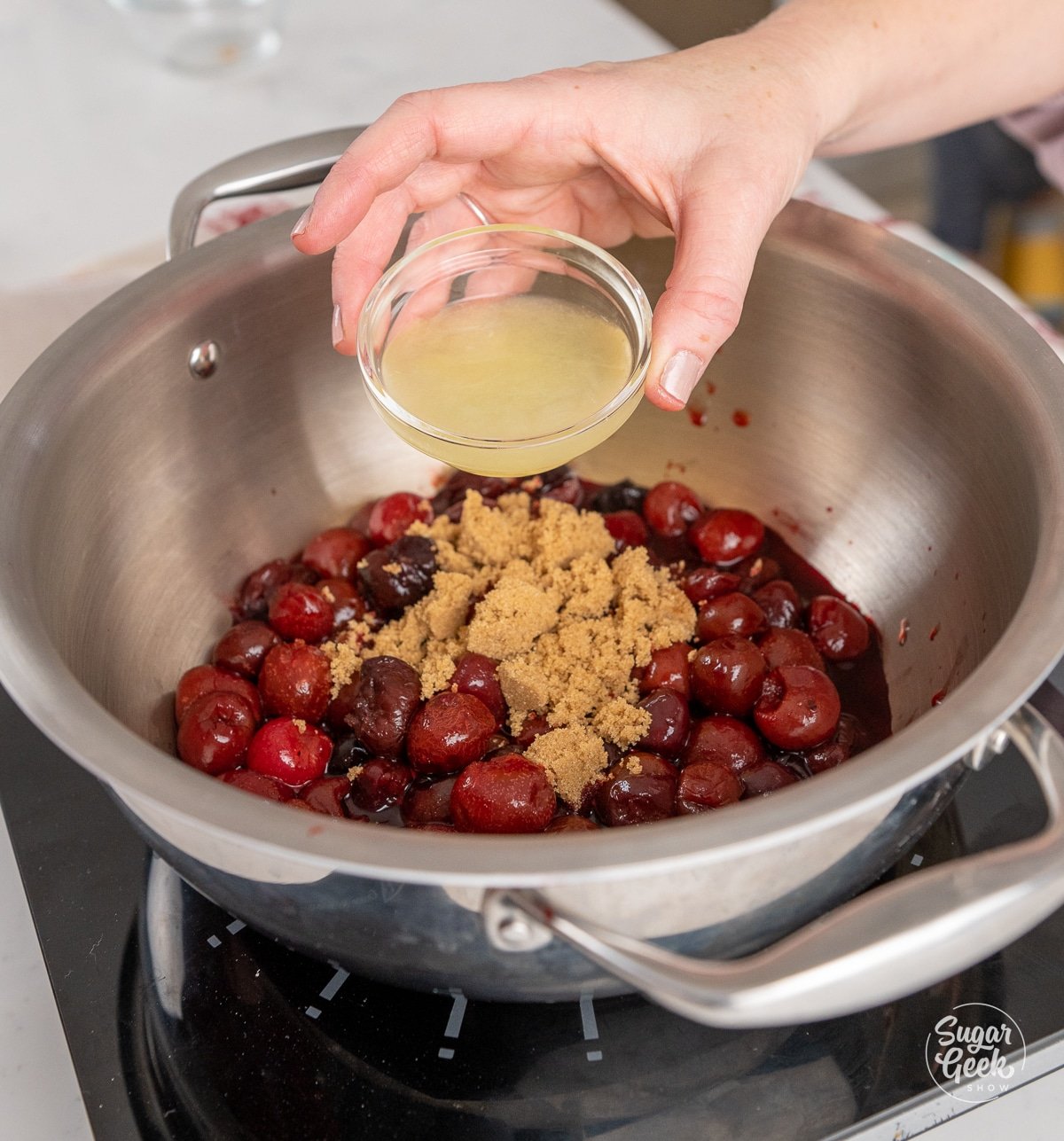 hand pouring a bowl of lemon juice into a pot with cherries