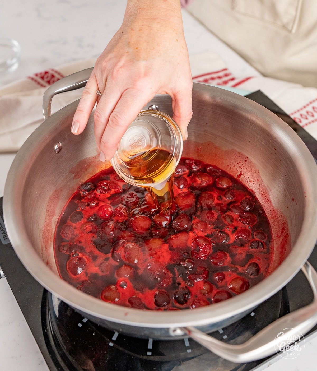 hand pouring a bowl of rum into a pot with cherries