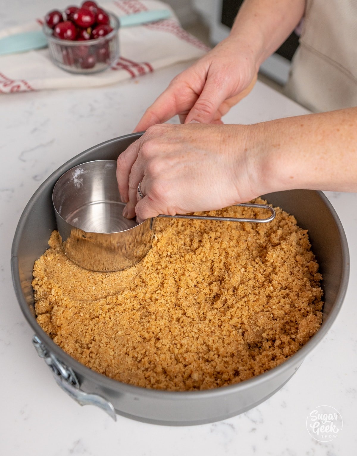 hand pressing a measuring cup onto the edges of a graham cracker crust