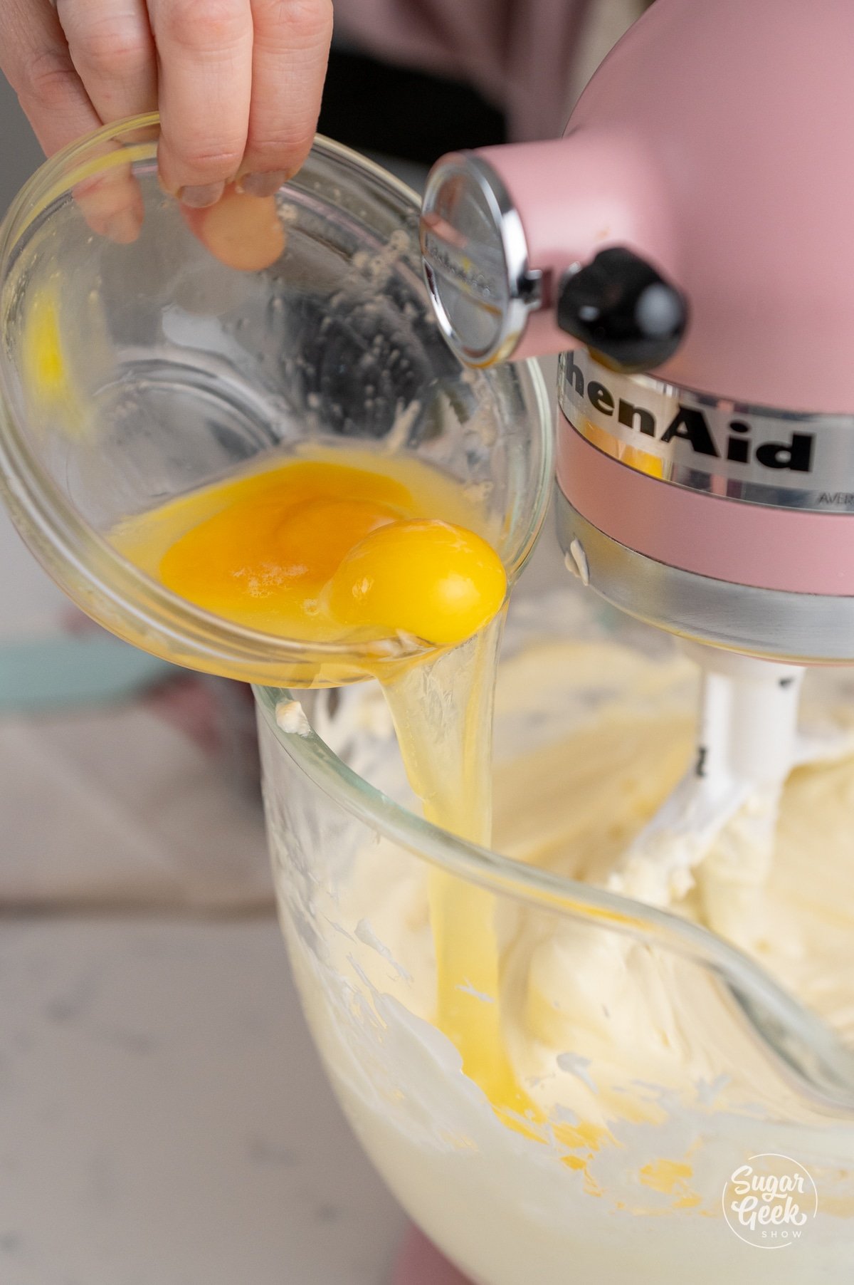 hand adding a bowl of eggs into a stand mixer bowl
