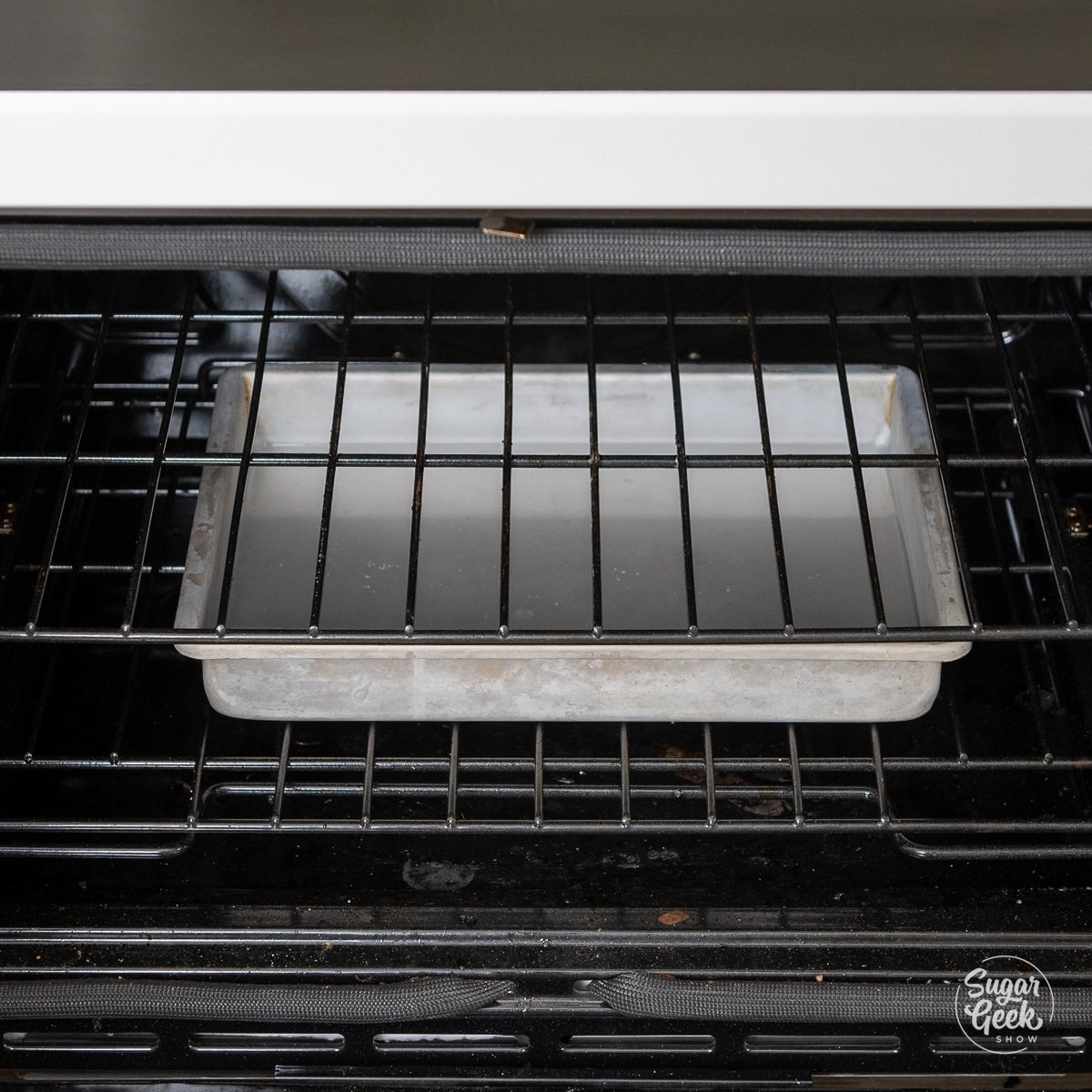 A rectangular cake pan full of water on the bottom rack of an oven