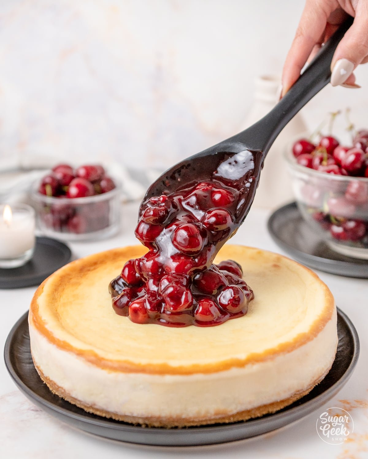 black spoon drizzling cherry filling on top of a cheesecake
