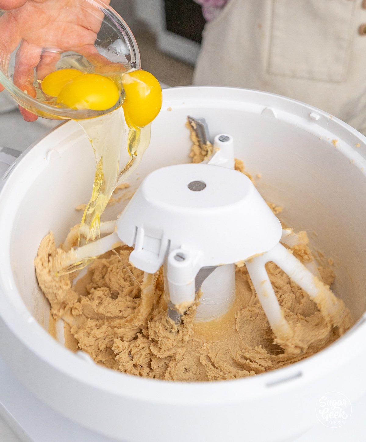 hand adding a bowl of eggs into a stand mixer bowl