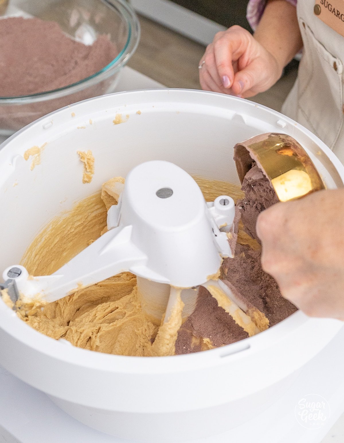 hand using a measuring cup to add dry ingredients to a stand mixer bowl