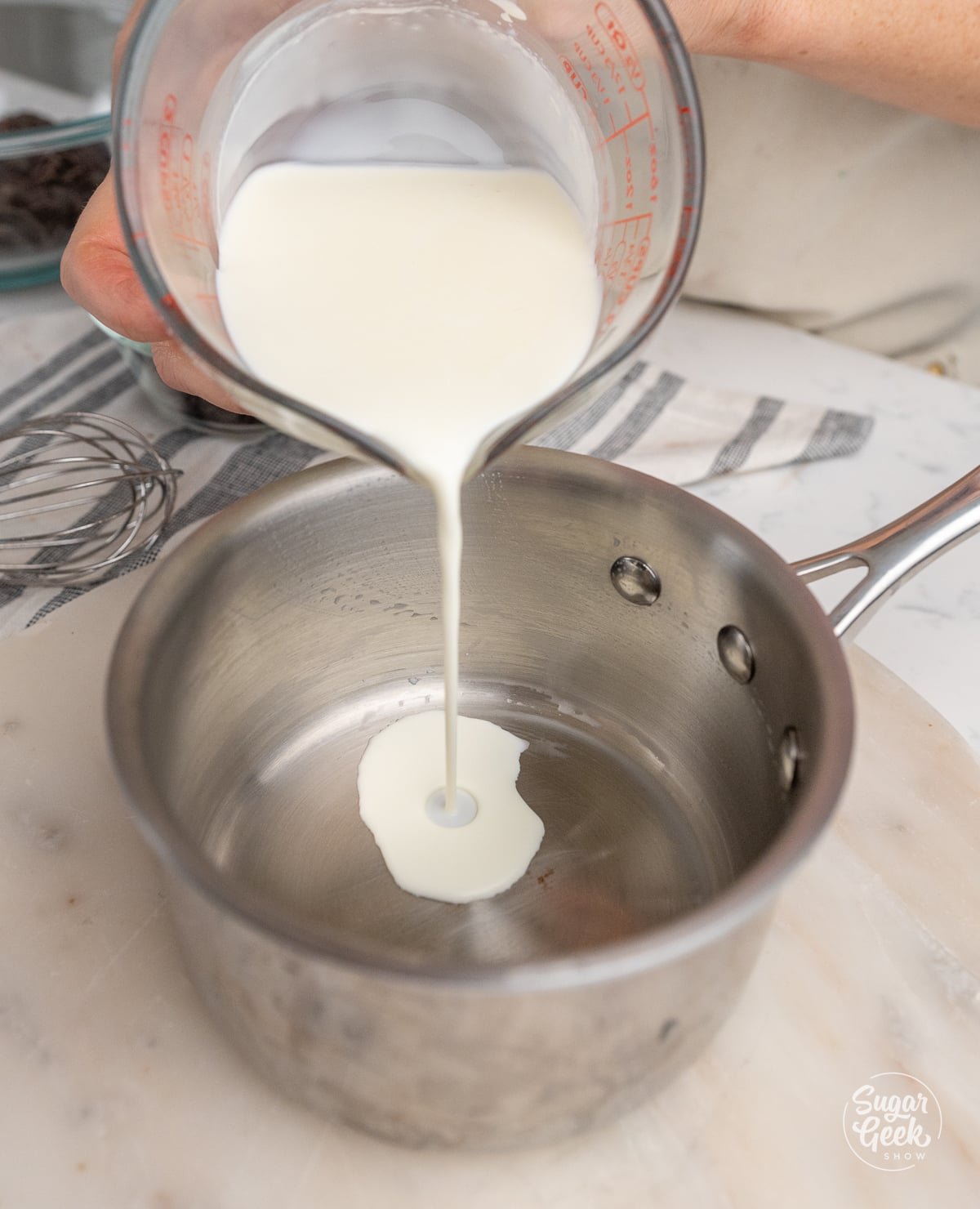 hands pouring a container of cream into a saucepan