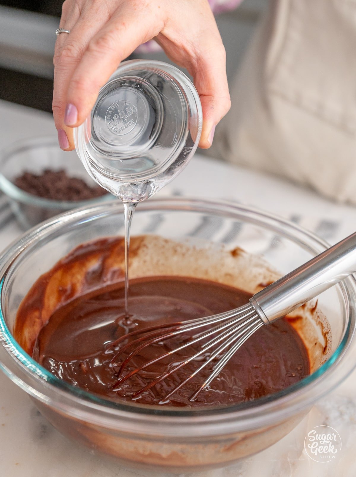 hand pouring a bowl of corn syrup into a bowl of ganache
