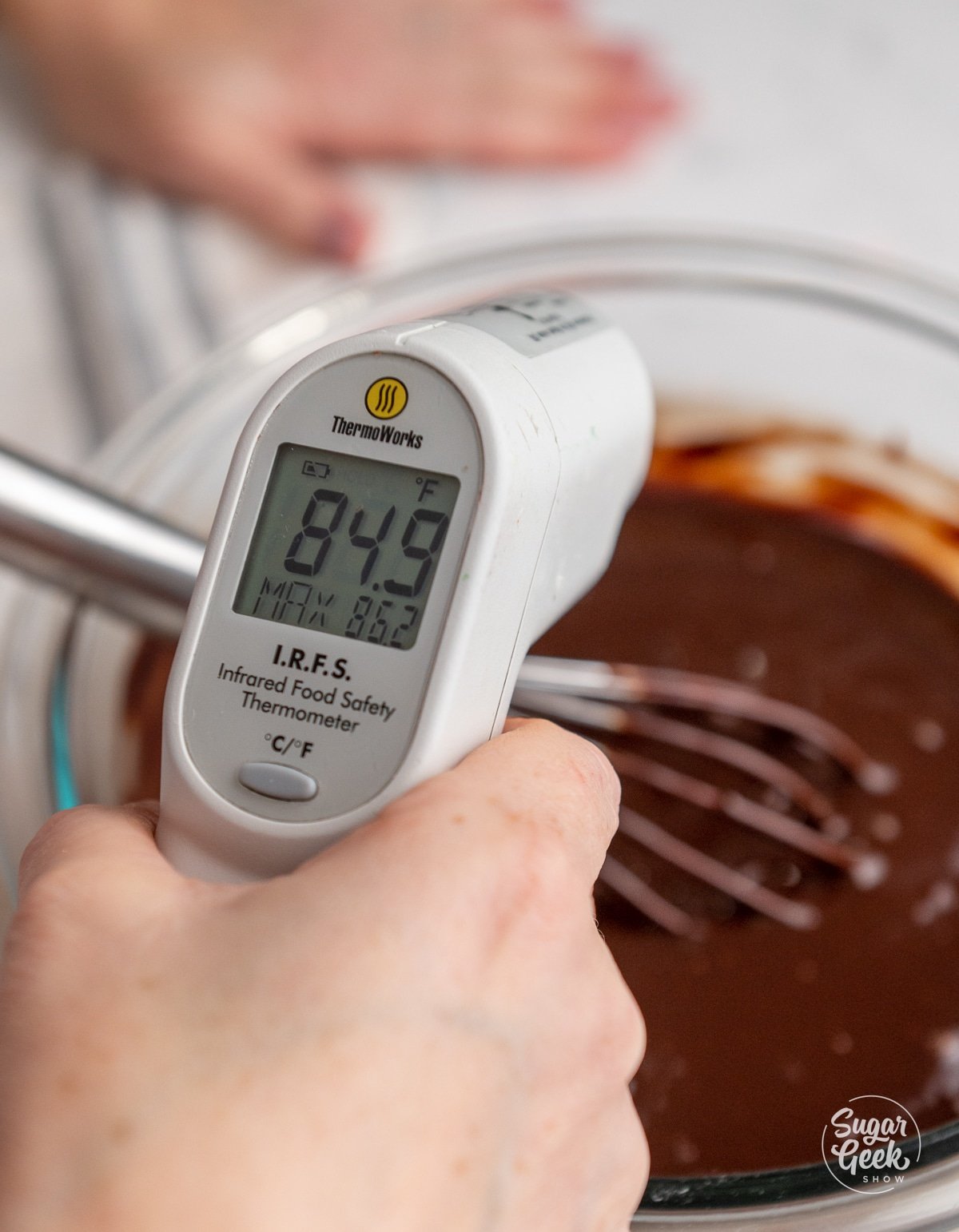 hand holding an instant thermometer to check the temperature of ganache