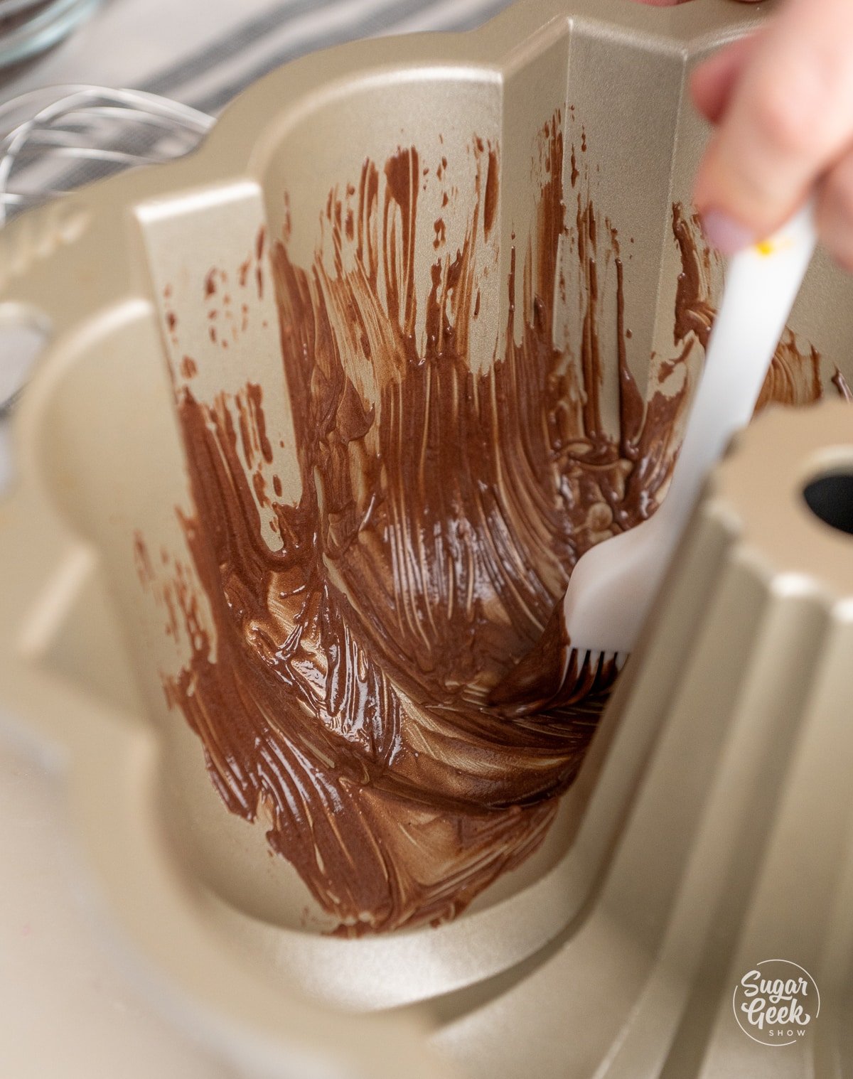 hand brushing chocolate cake goop into a bundt cake pan