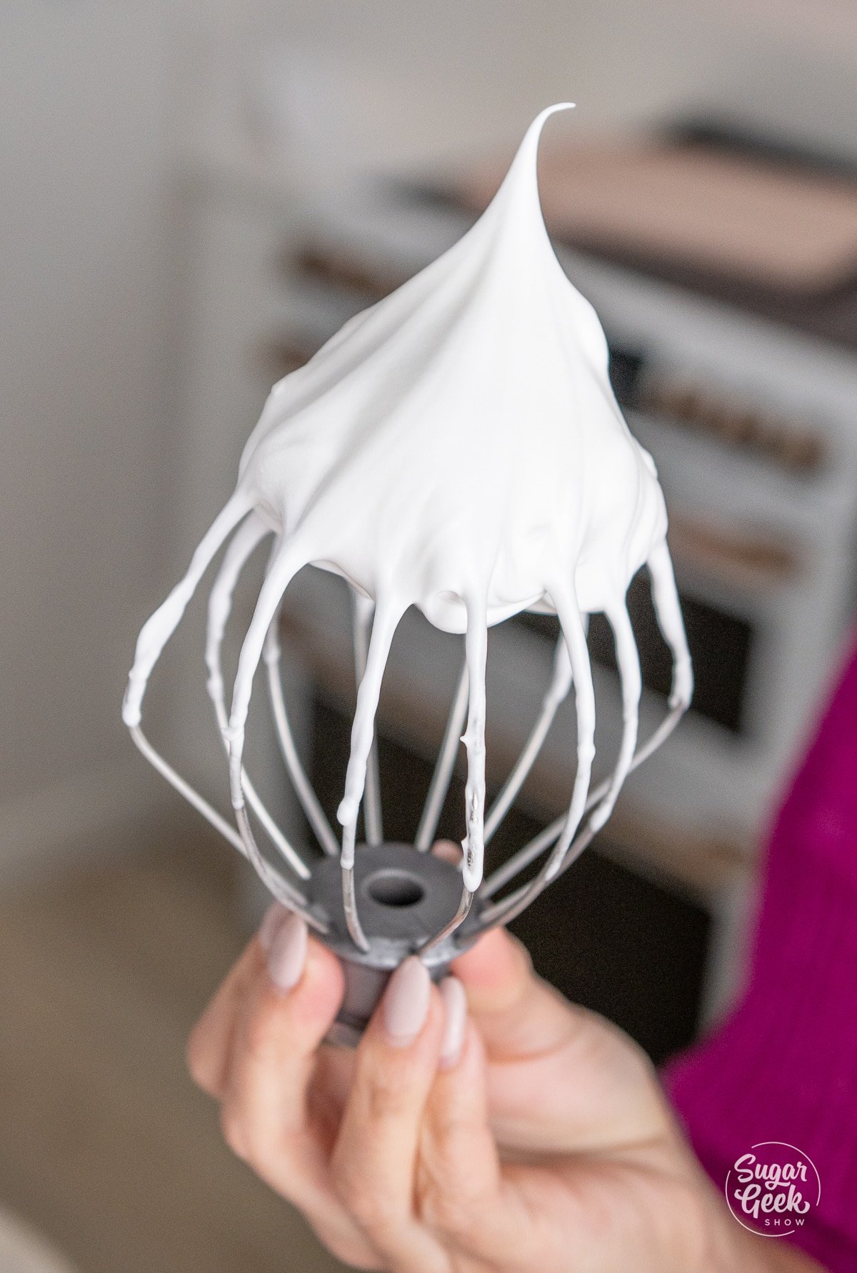 hand holding a whisk of meringue at a stiff peak