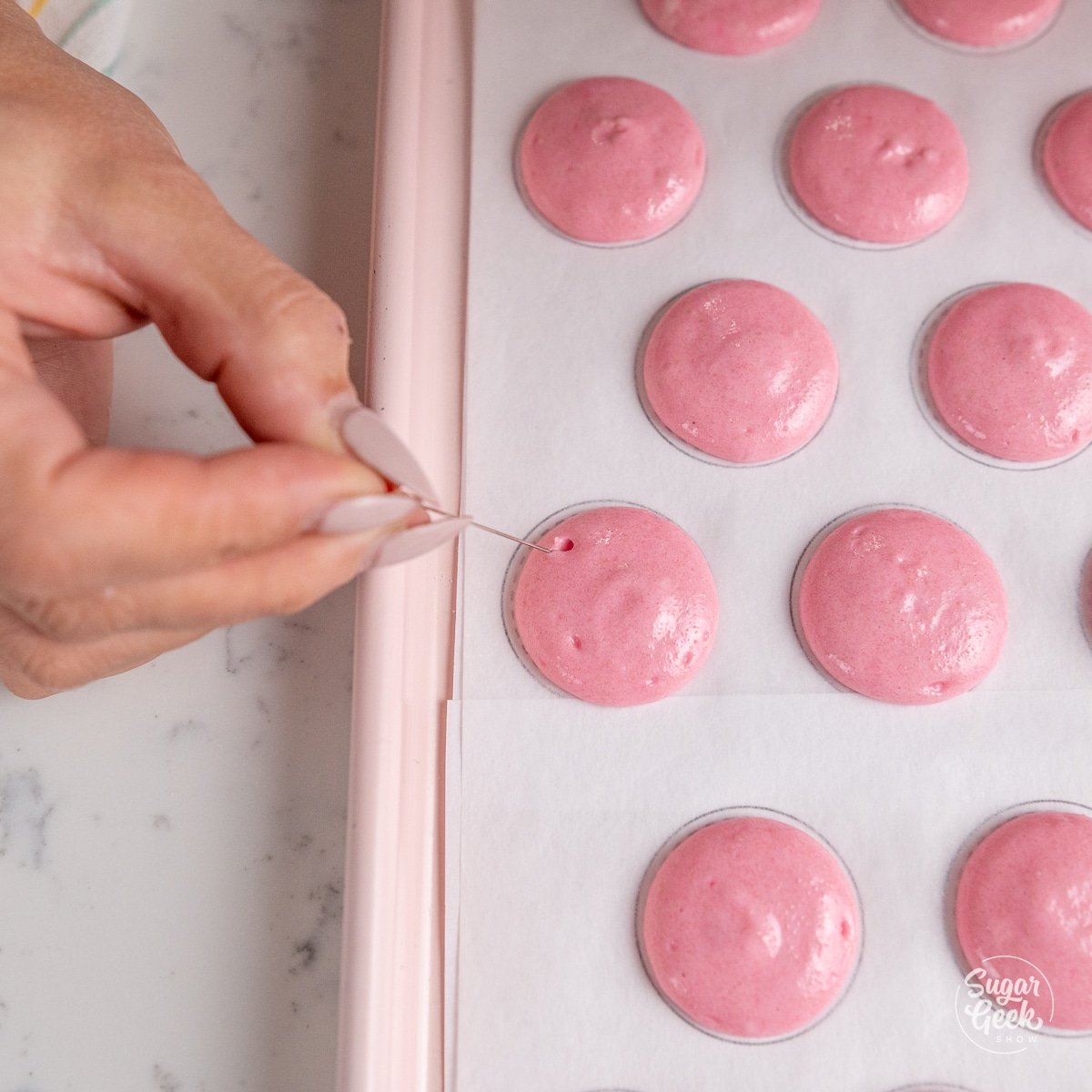 hand holding a needle above unbaked macarons