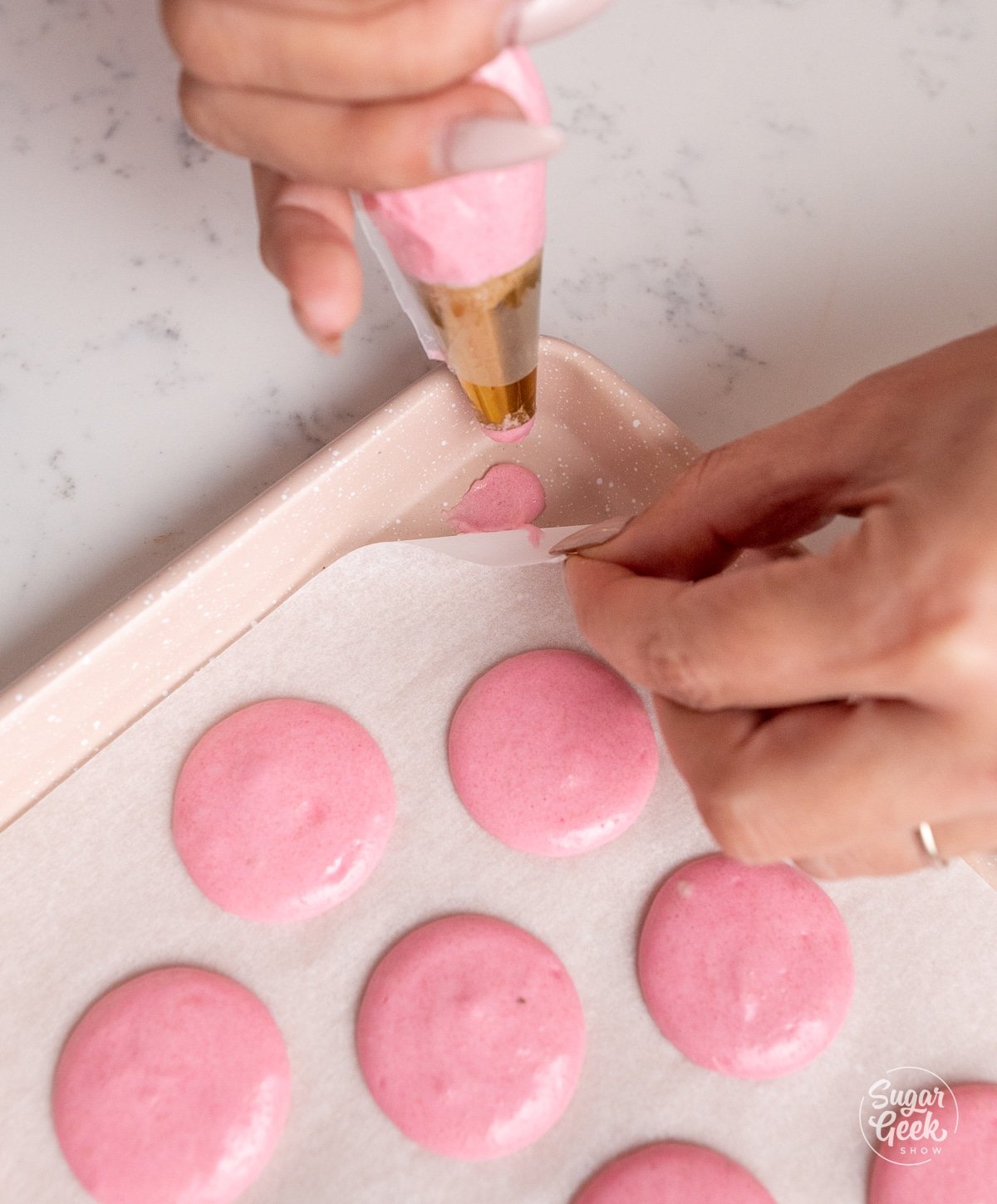 hands piping a dot of macaron batter in the corner of a baking sheet