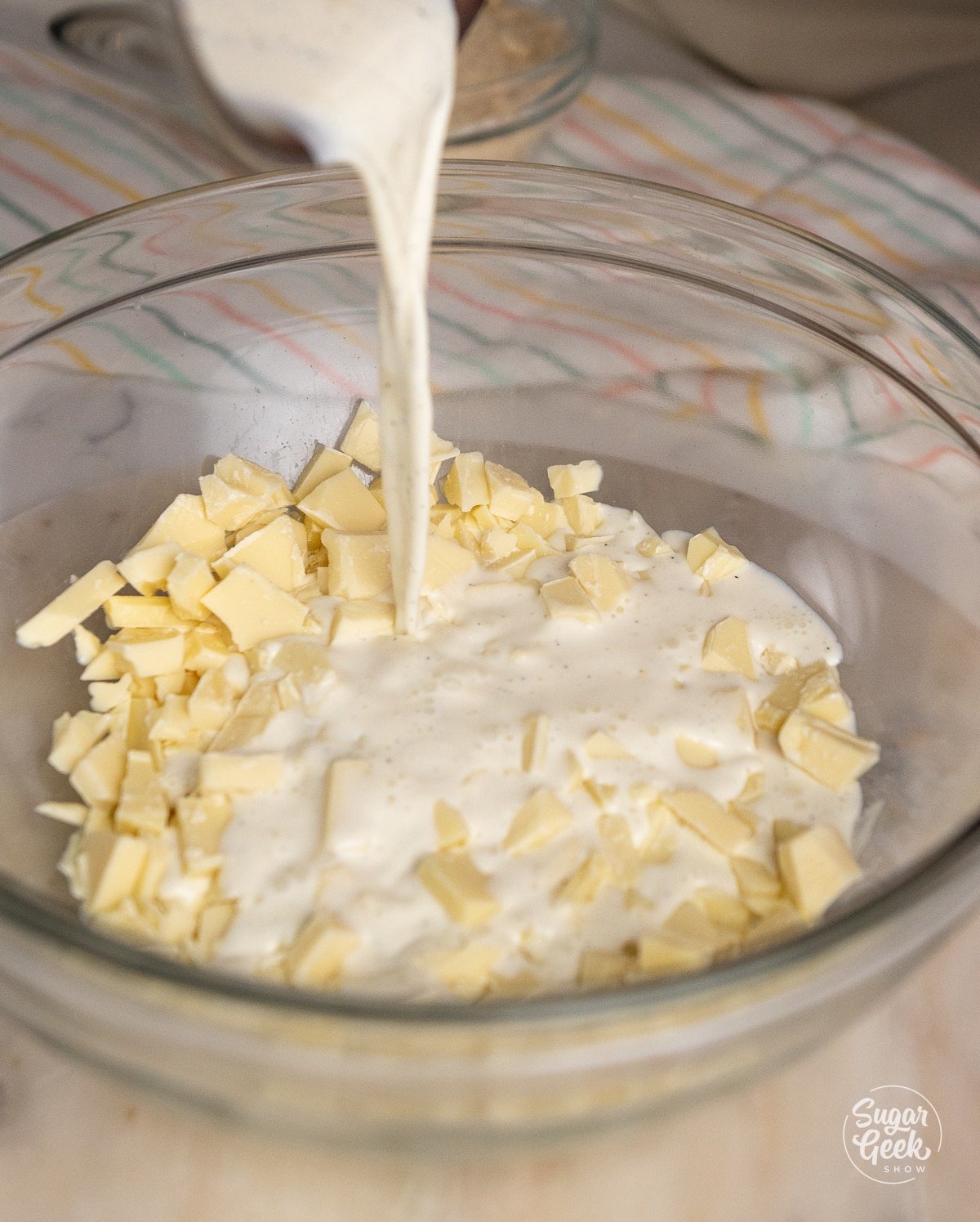 container pouring cream into a bowl of chopped white chocolate