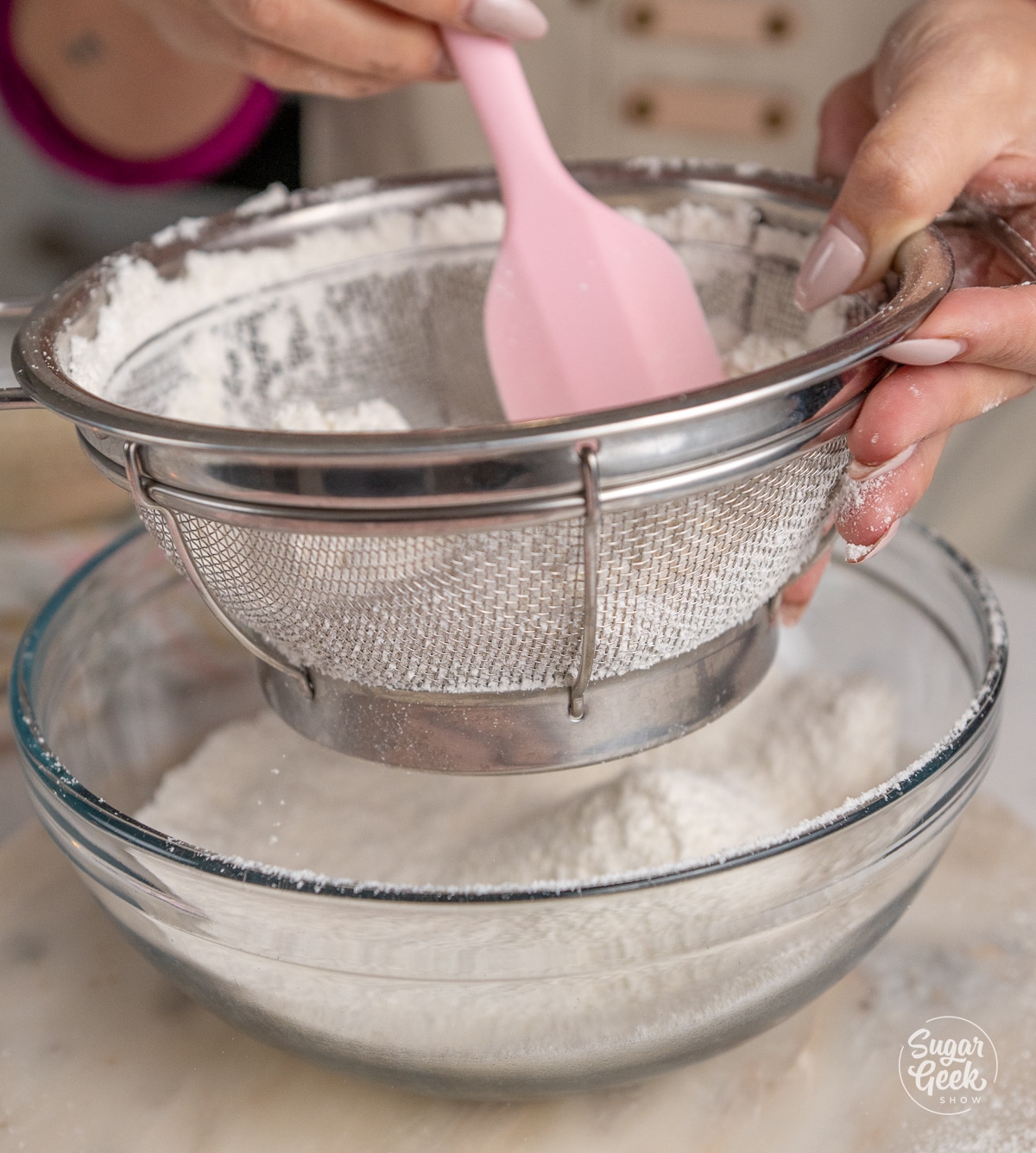 hands pushing dry ingredients through a sifter with a spatula