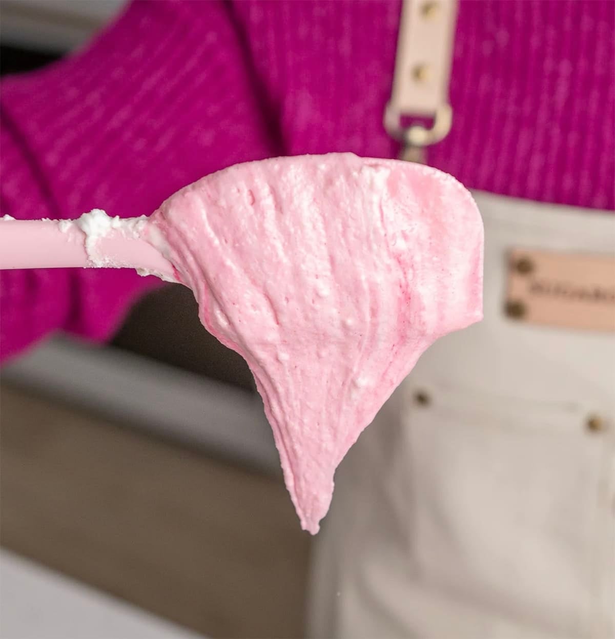 Macaron batter flowing off a pink spatula in a "V" shape.