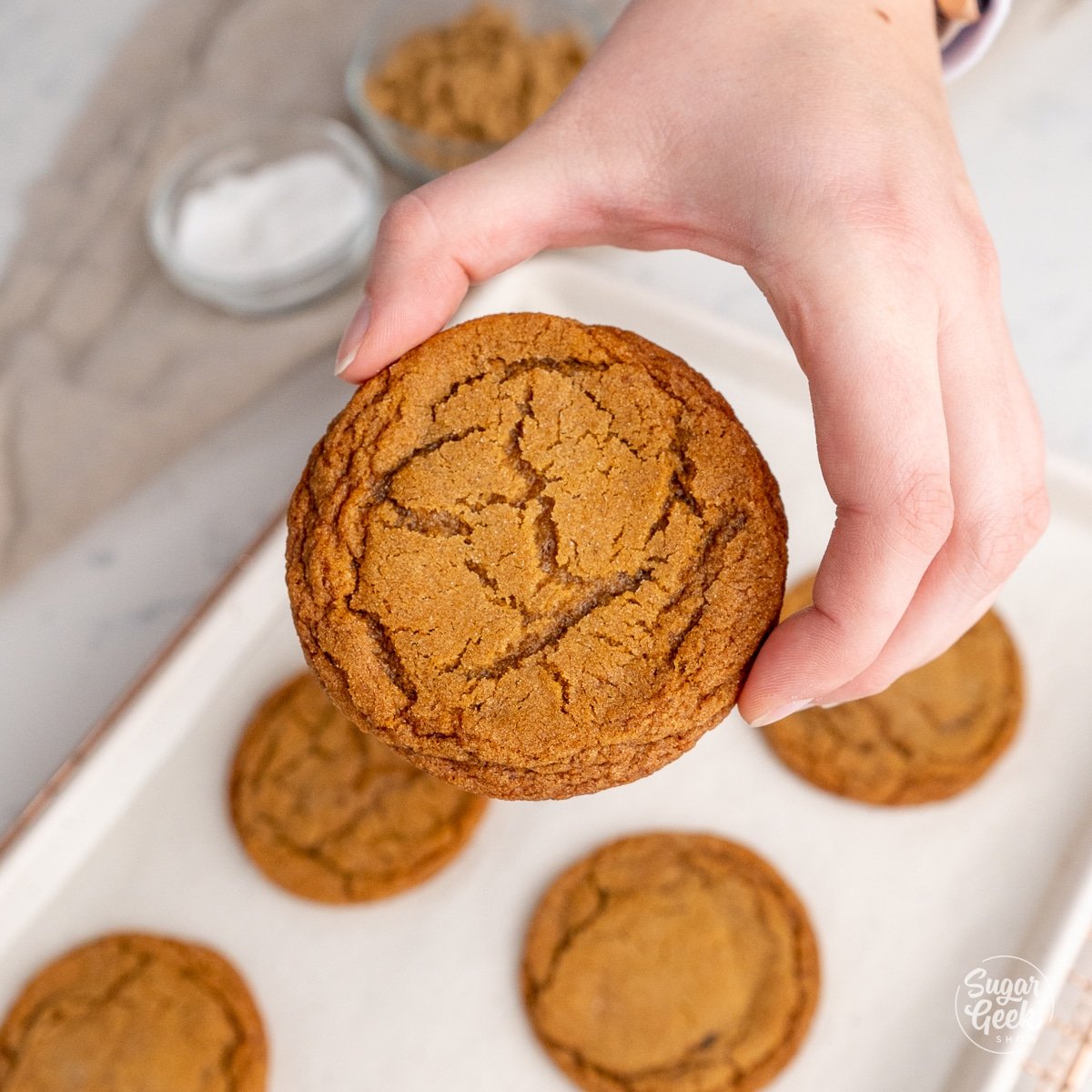 hand holding a molasses cookie above a sheet pan