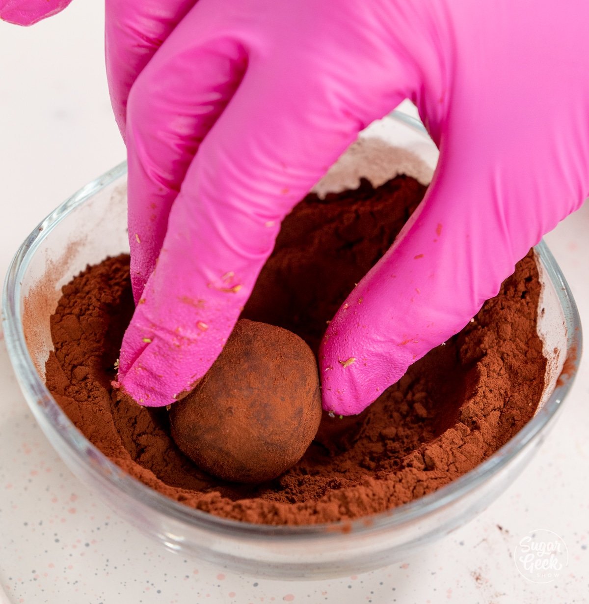 gloved hand rolling a ganache truffle in cocoa powder