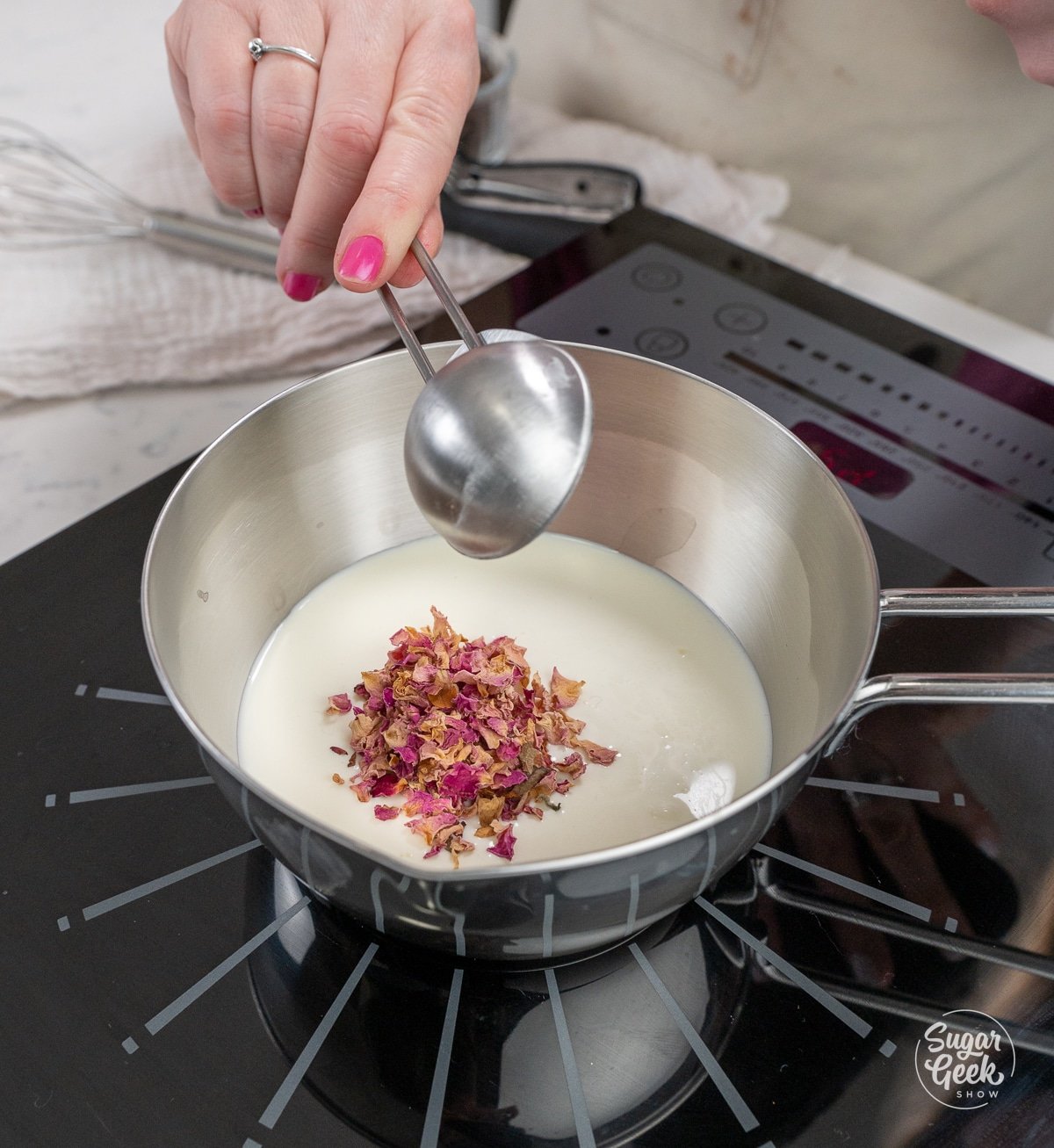 hand adding a tablespoon of rose petals to a saucepan of cream