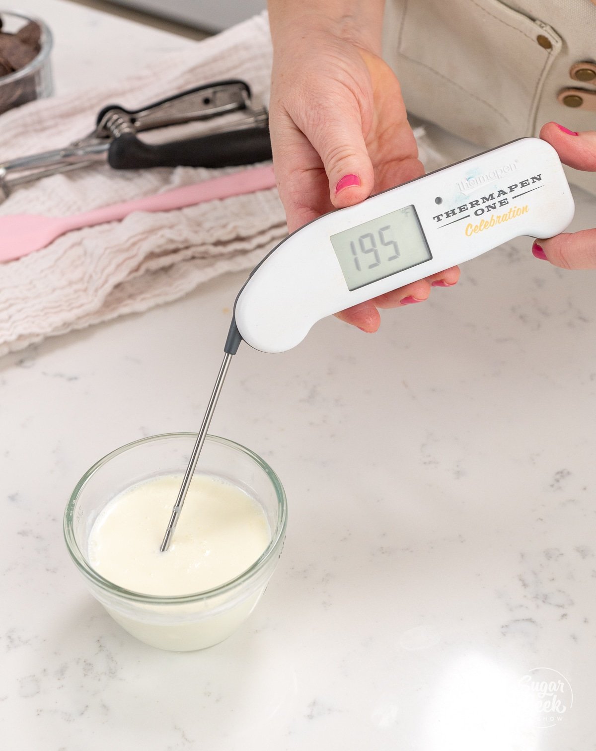 hand getting the temperature of a bowl of cream with a thermometer