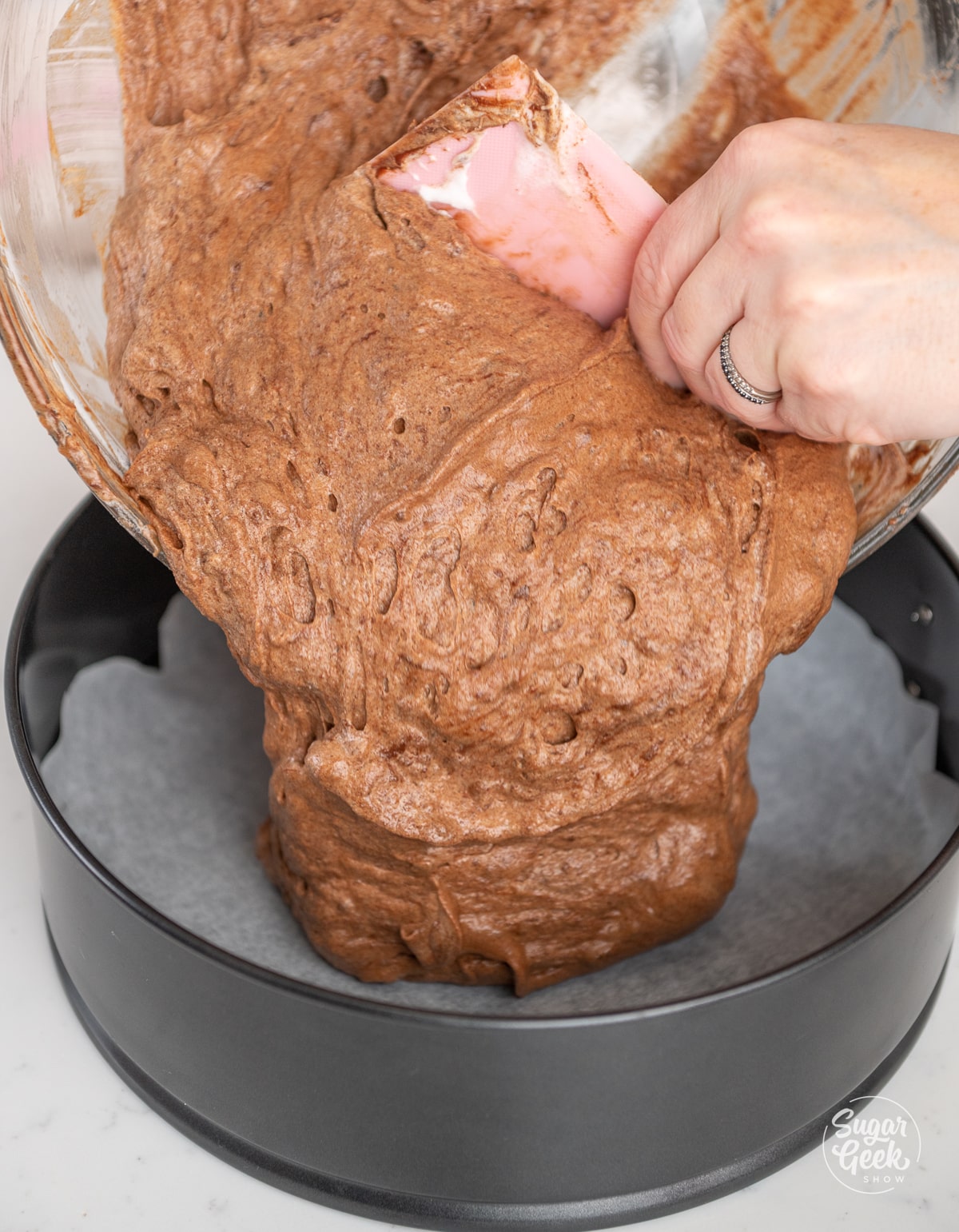 bowl of chocolate cake batter pouring into a springform pan