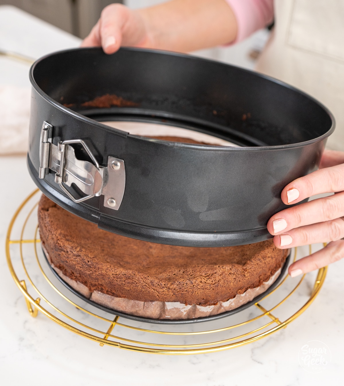 hands removing a springform pan from the outside of a flourless chocolate cake