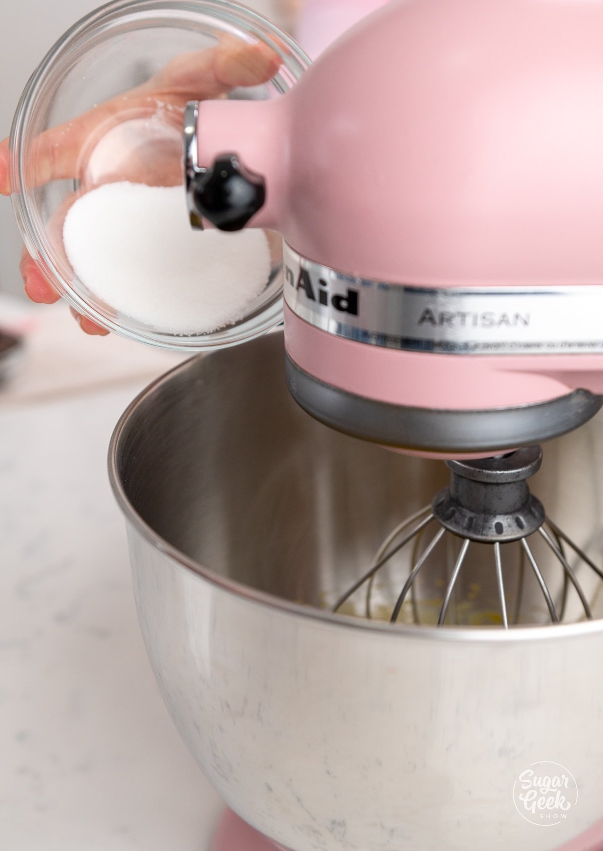 hand adding a bowl of sugar into a stand mixer bowl