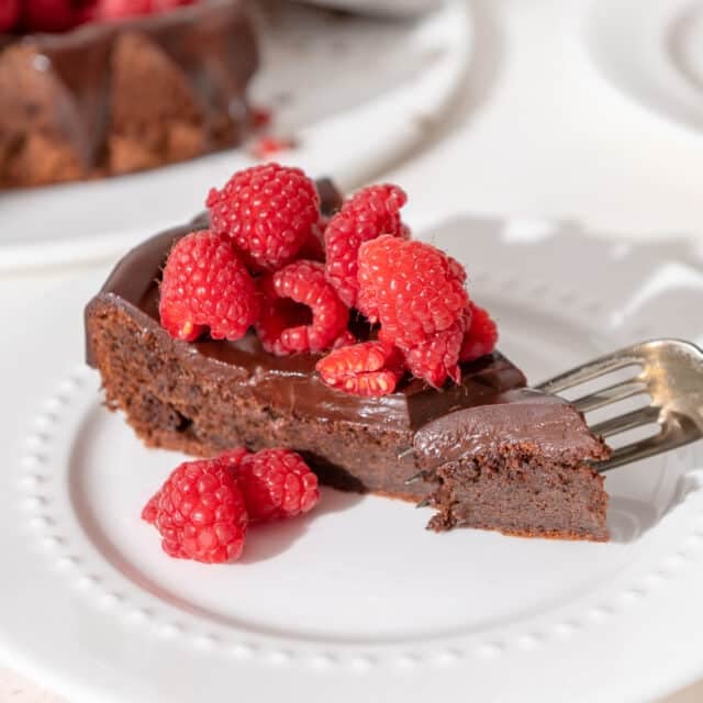 slice of flourless chocolate cake on a plate with raspberries on top