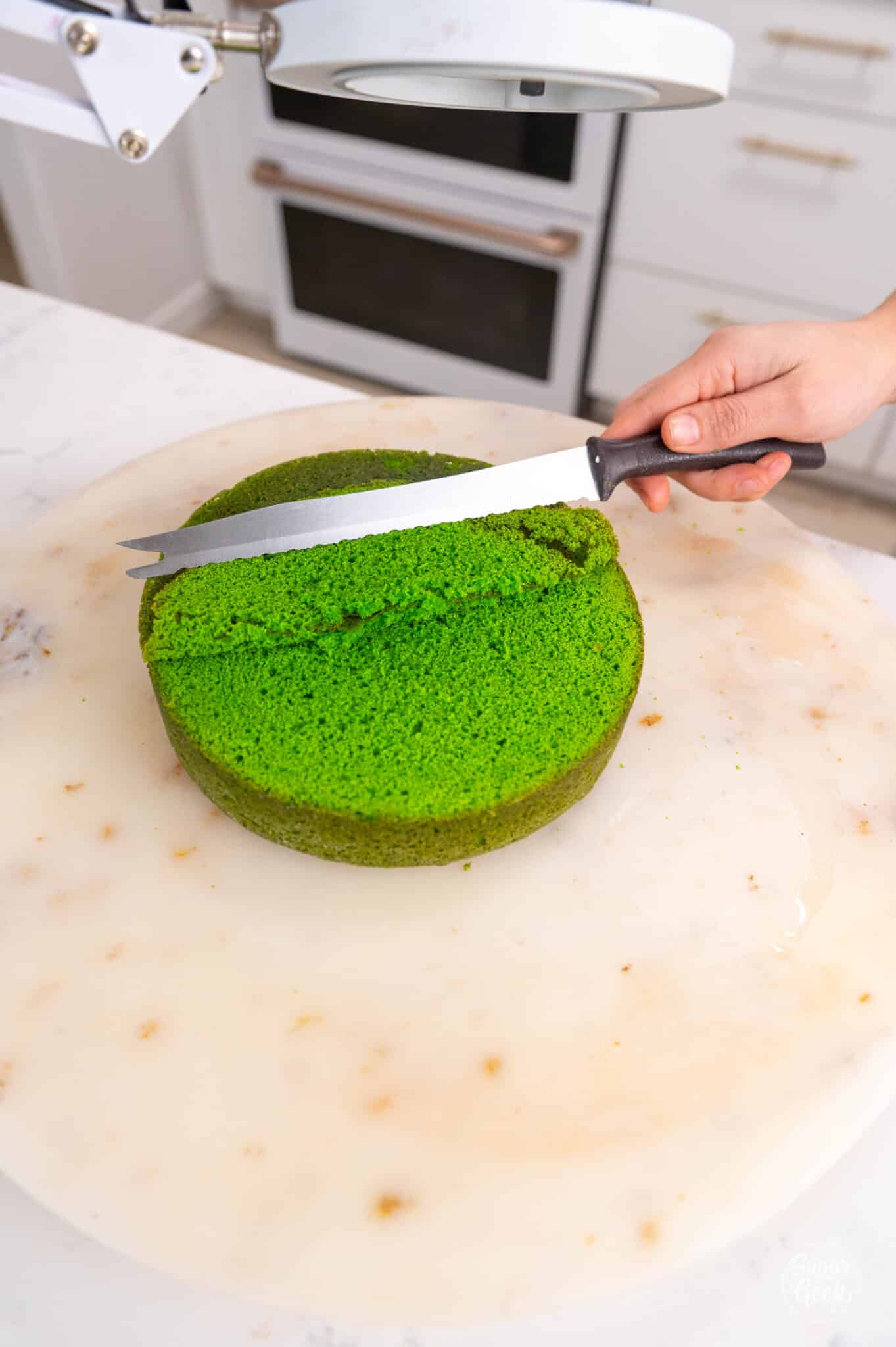 hand cutting off the top dome of a green velvet cake with a knife