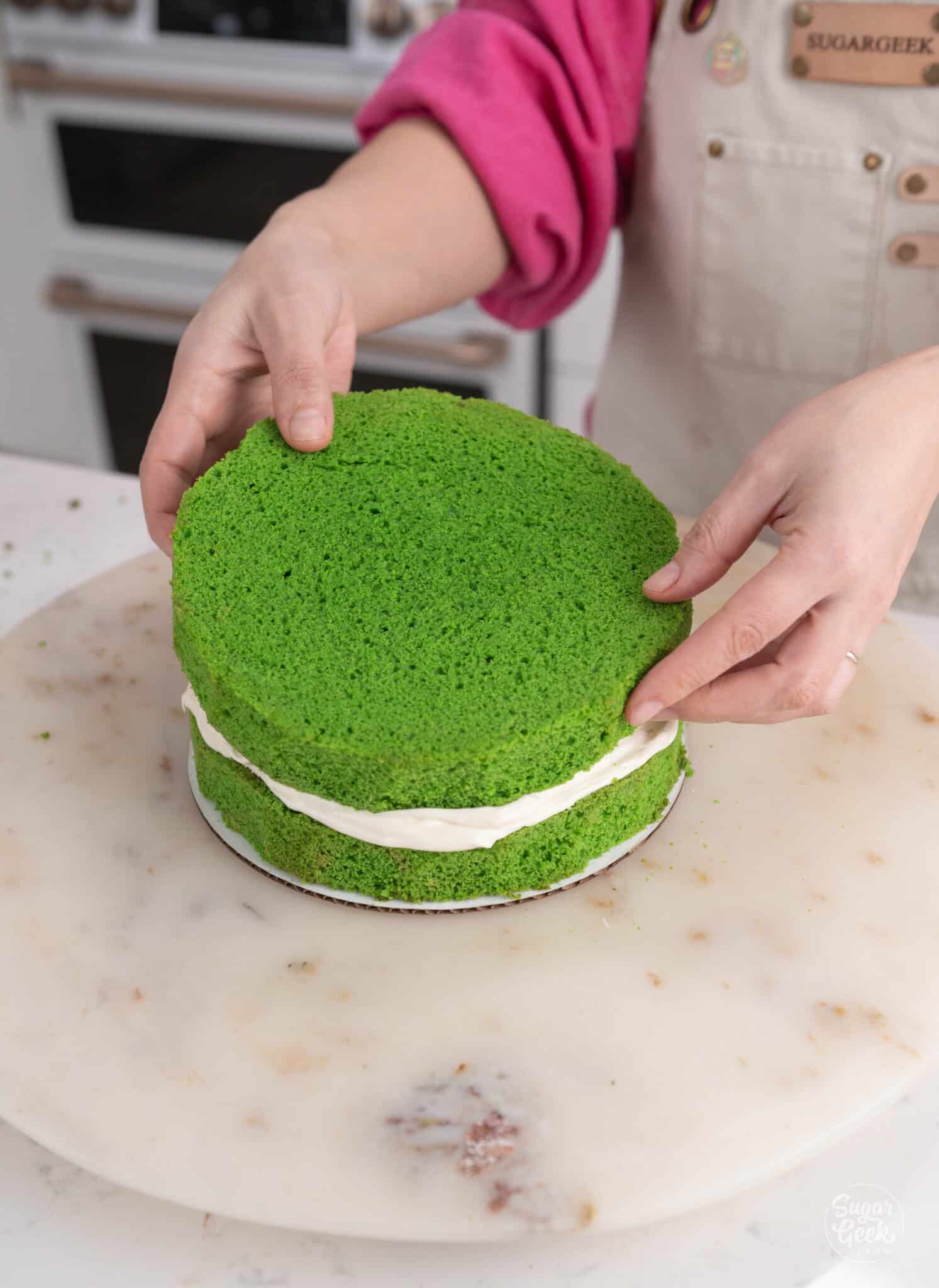 hands placing a second later of green cake on top of the first