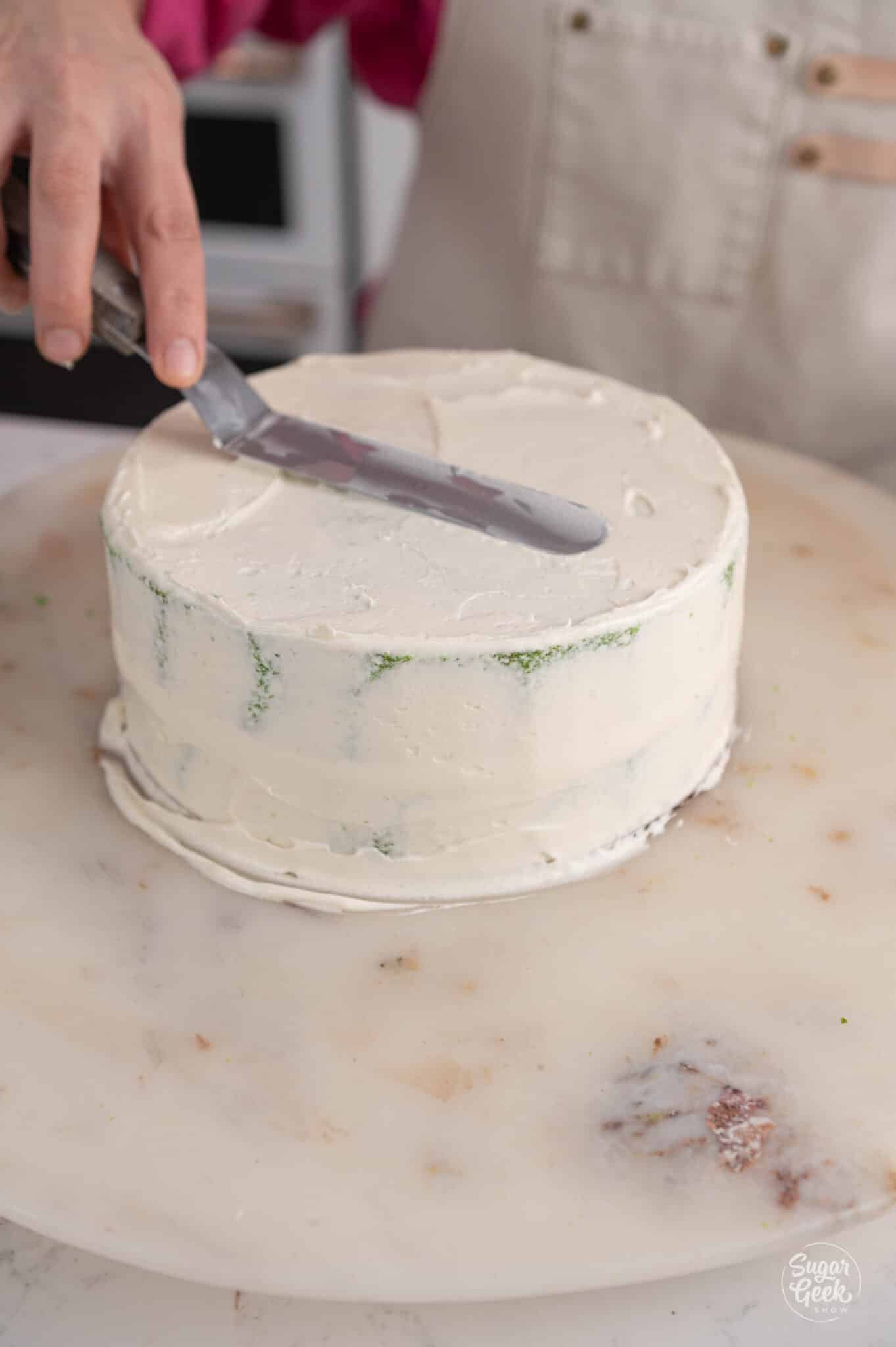 smoothing a crumb coat on a green velvet cake with a spatula