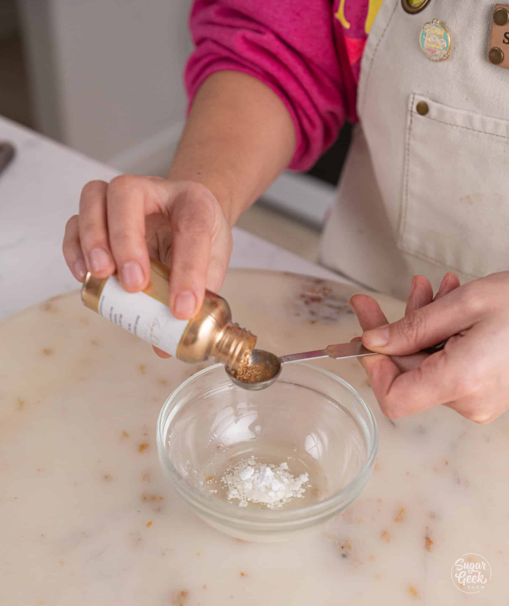 hands measuring out gold dust into a small glass bowl