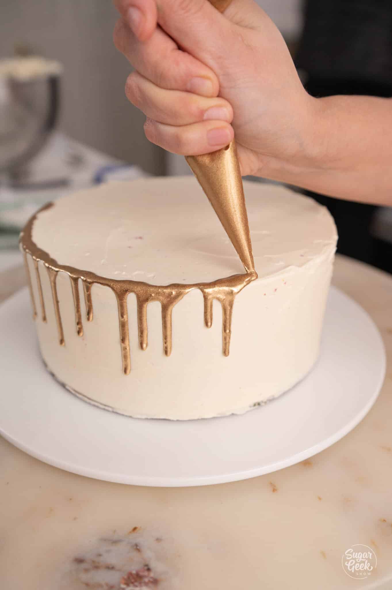 hand piping gold drip onto a chilled white cake