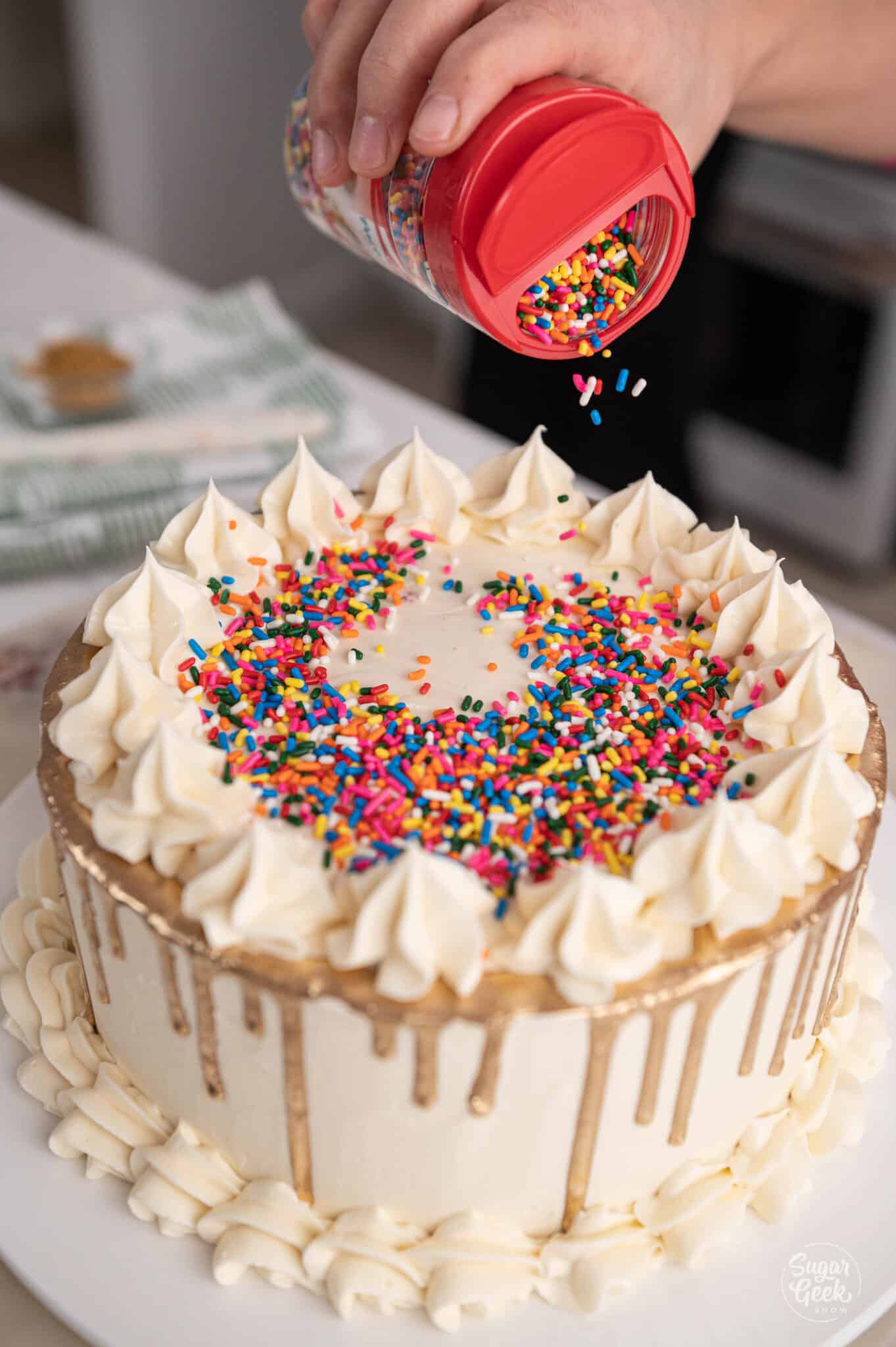 container of sprinkles pouring into the center of a cake