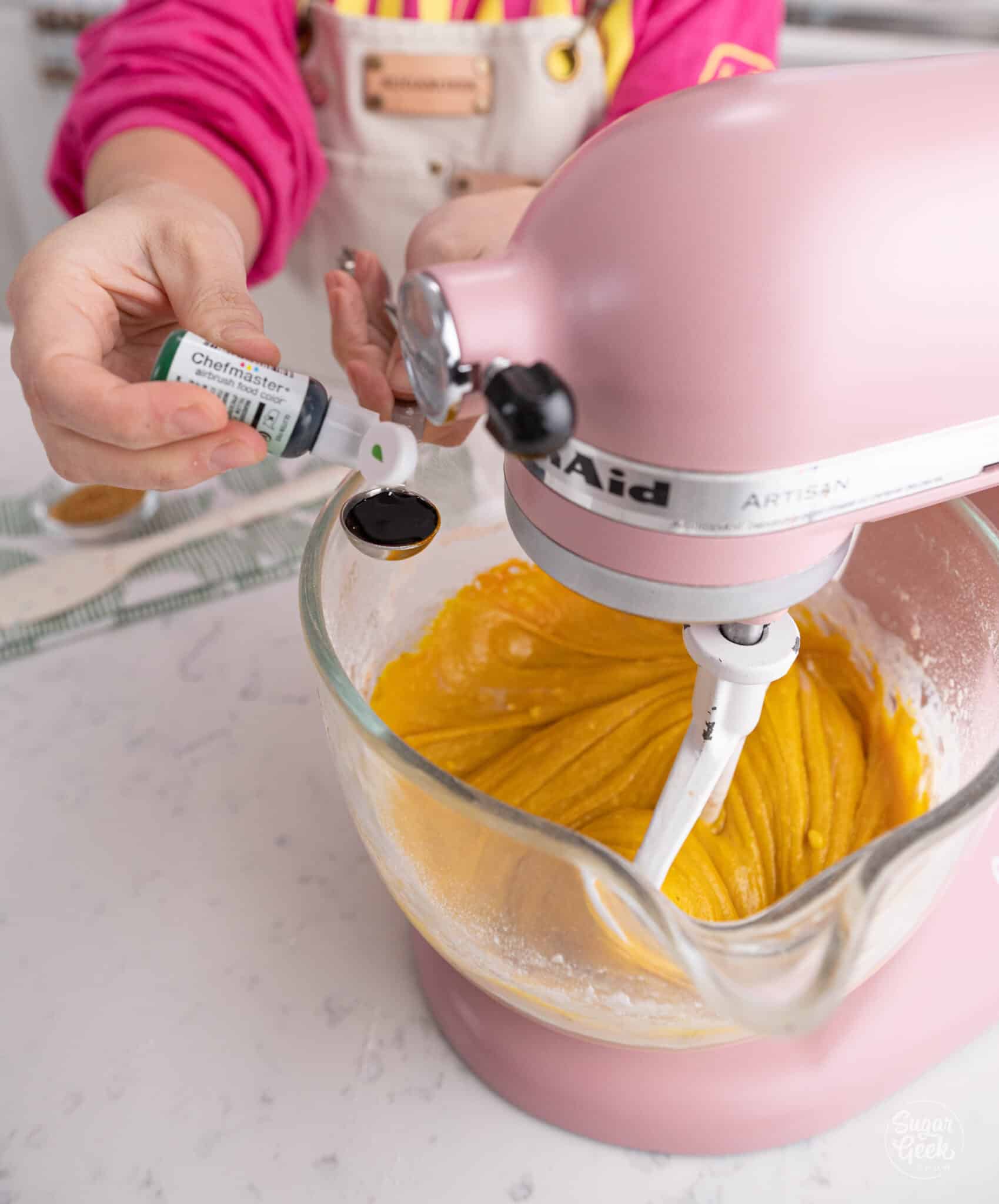 hand adding green food coloring to a stand mixer bowl