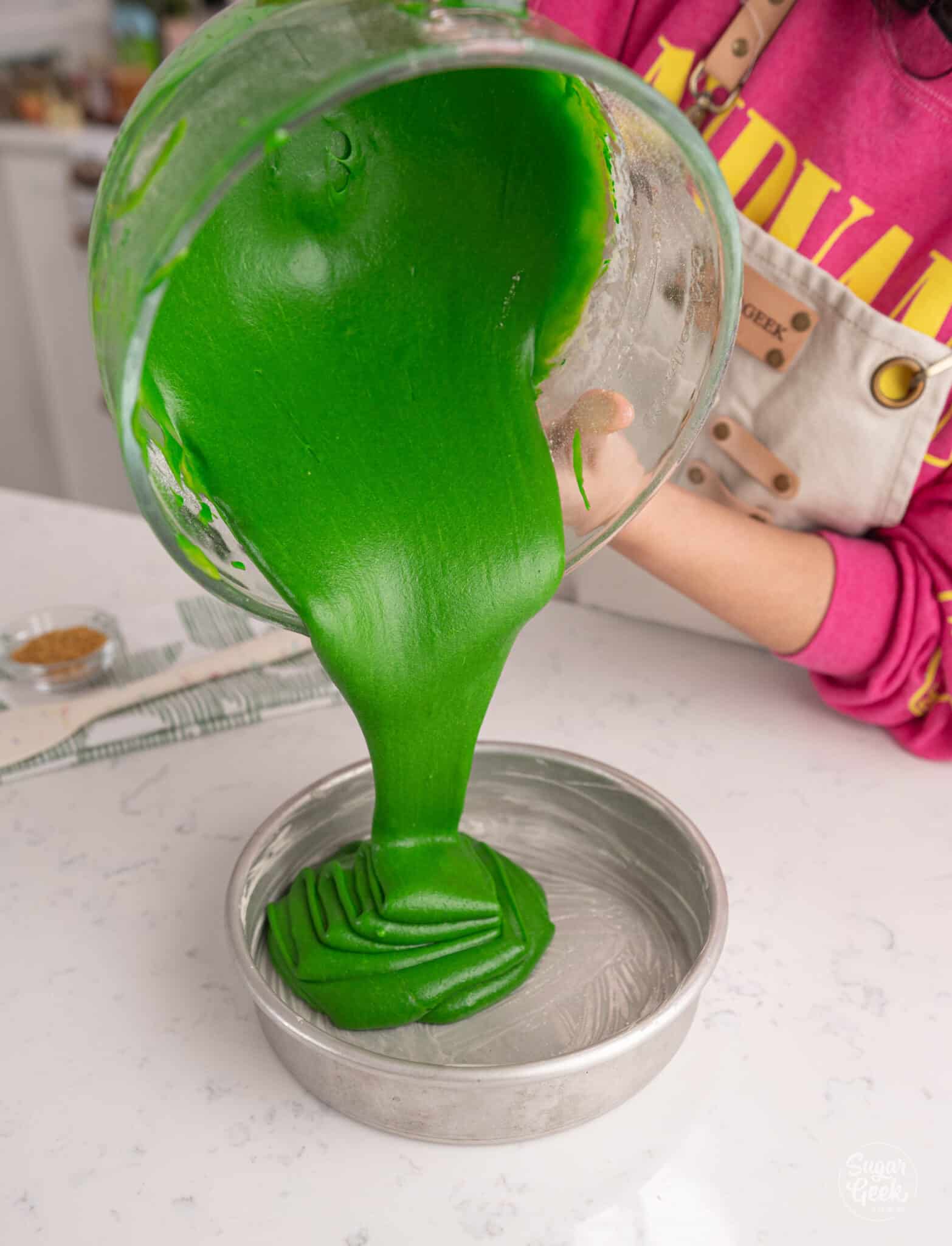 hands pouring green cake batter from a glass bowl into cake pans