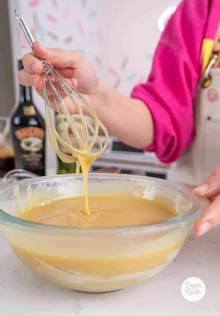 hand holding a whisk above a bowl of white chocolate ganache