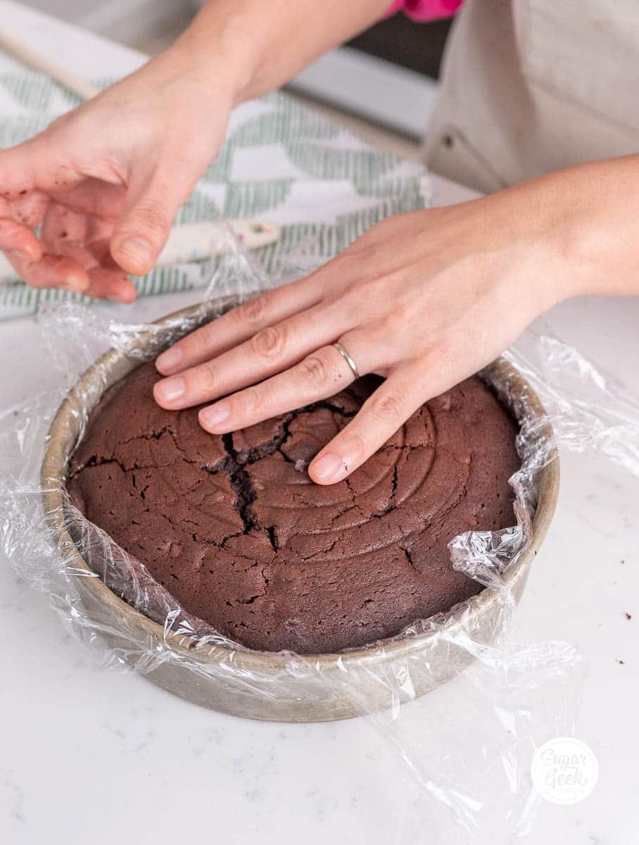 hands placing plastic wrap inside the pan and the cake on top