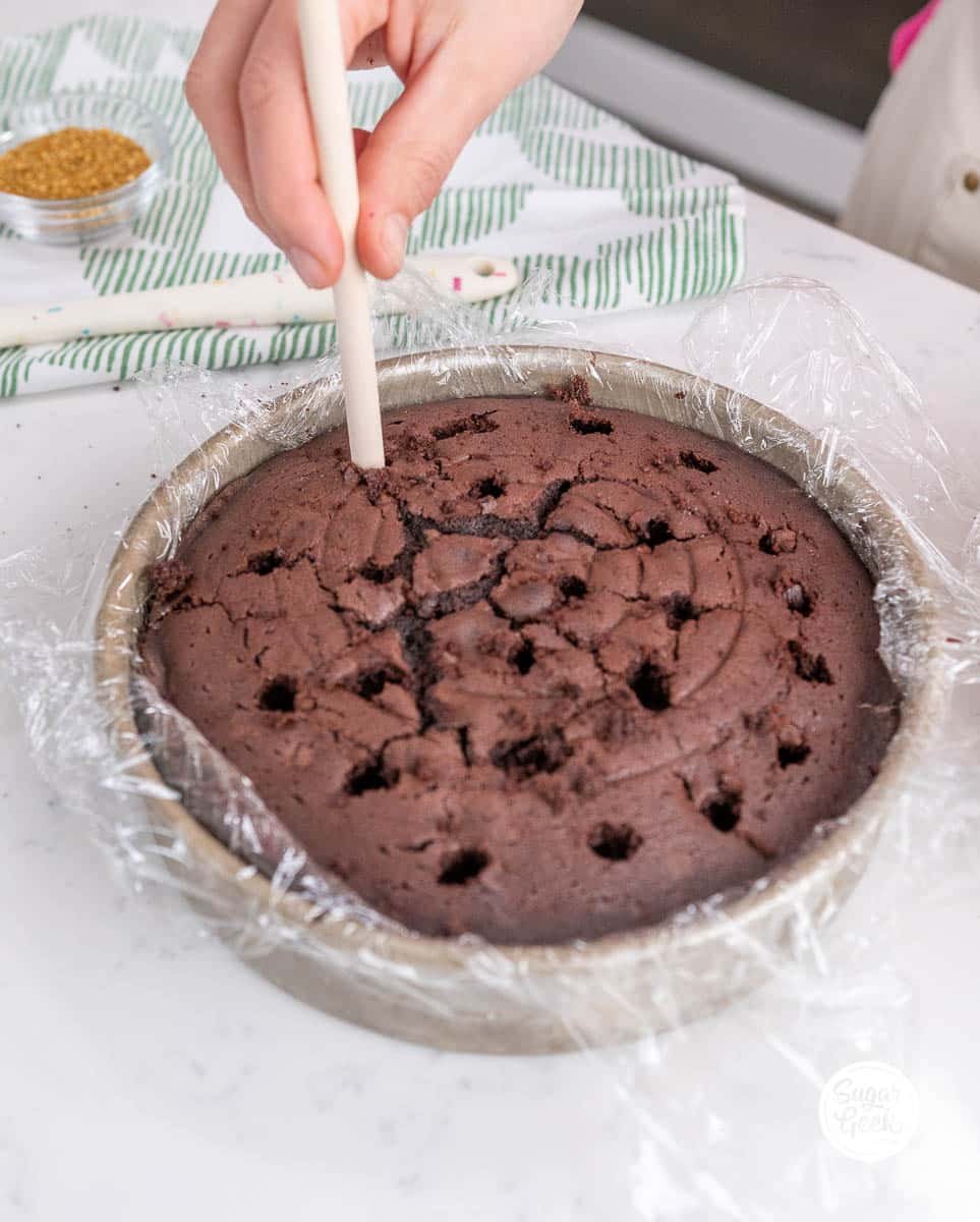hands poking holes into the top of the chocolate cake