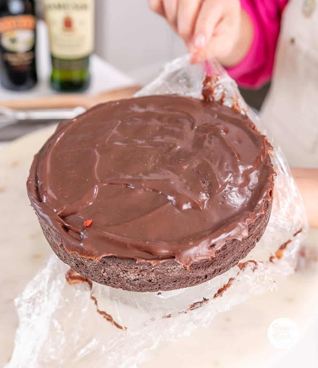 hands peeling plastic wrap off of a chilled chocolate cake