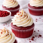 close up of a red velvet cupcake with cream cheese frosting piped on top surrounded by other cupcakes