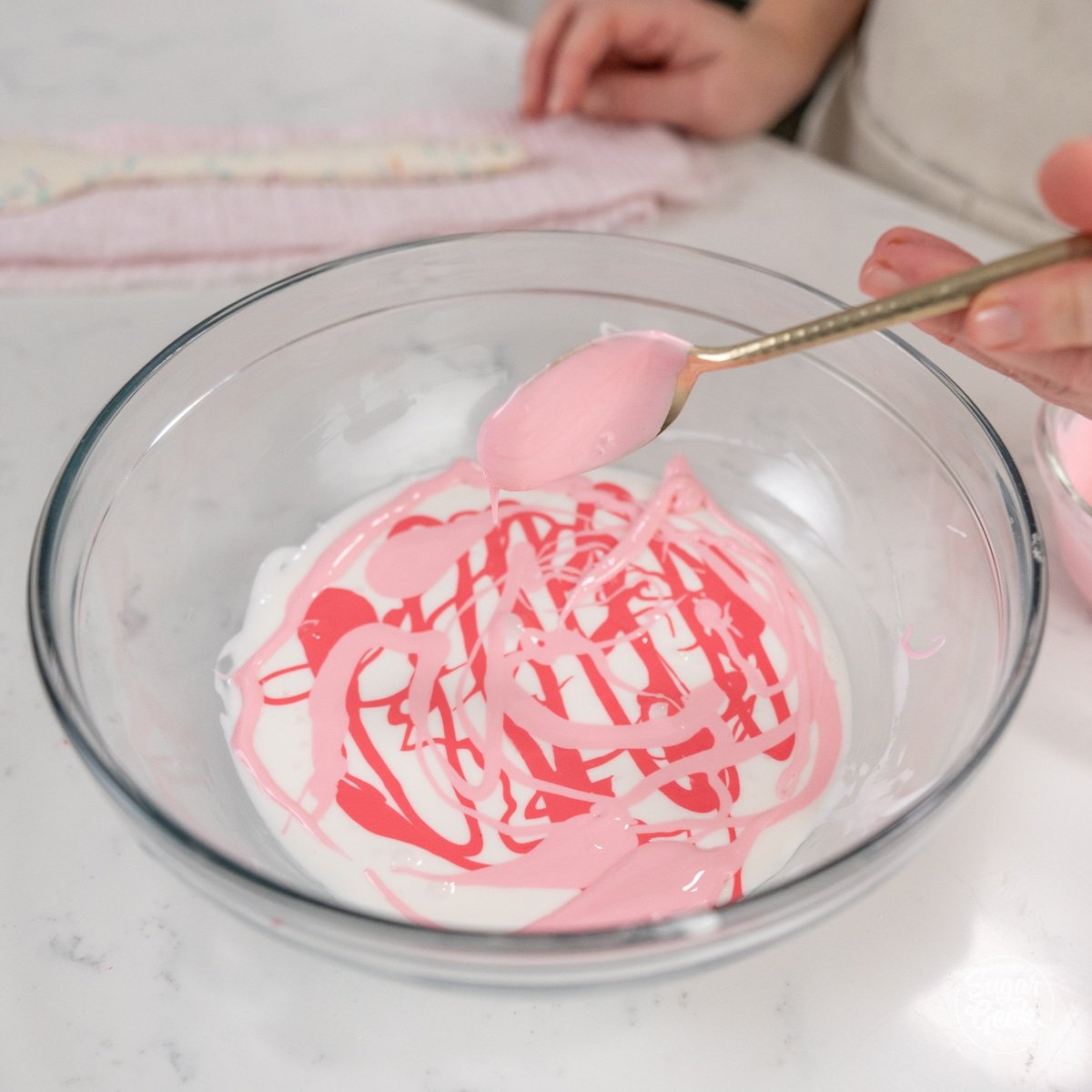 hand using spoon to drizzle colored icing over white icing.