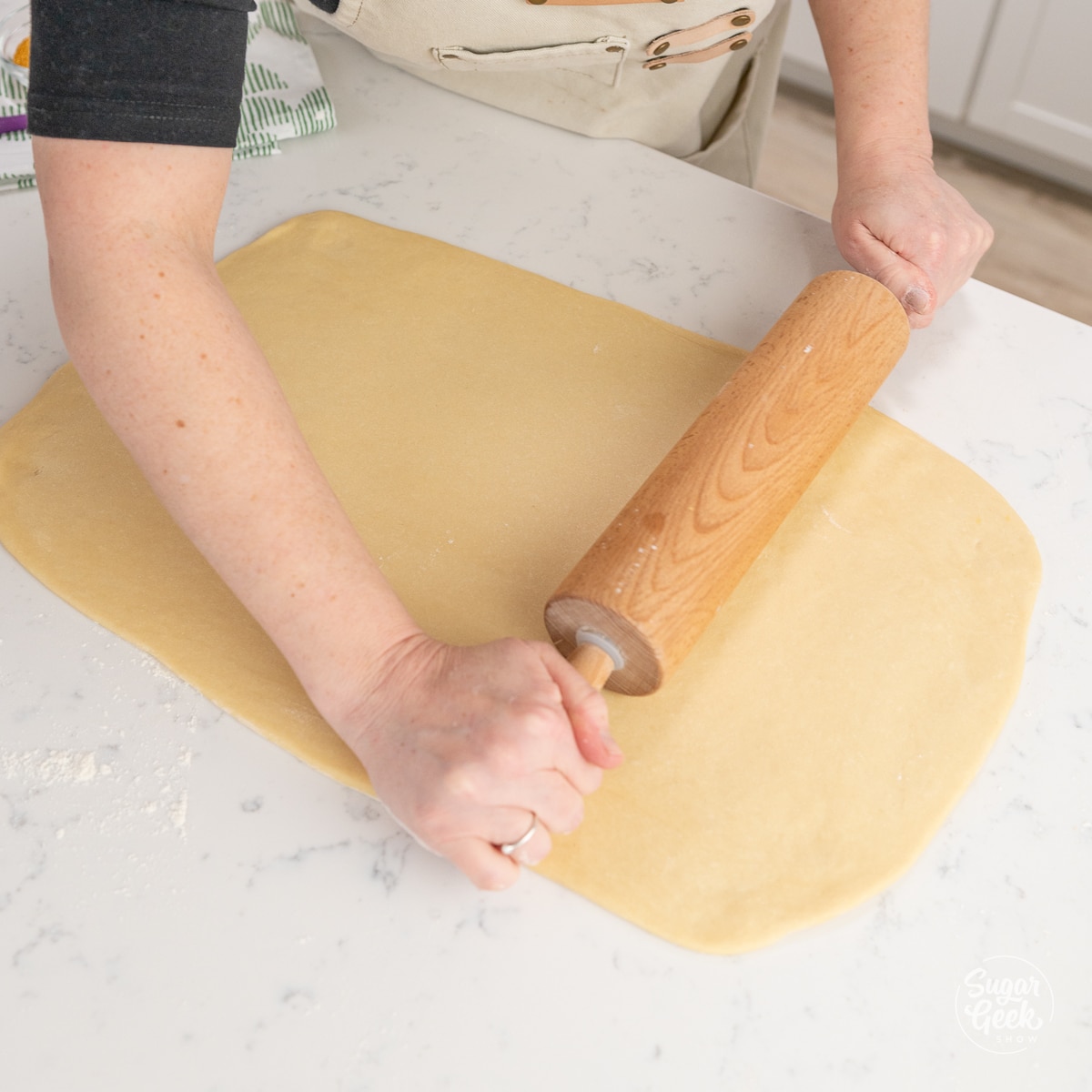 hands rolling out dough in a rectangle with a rolling pin