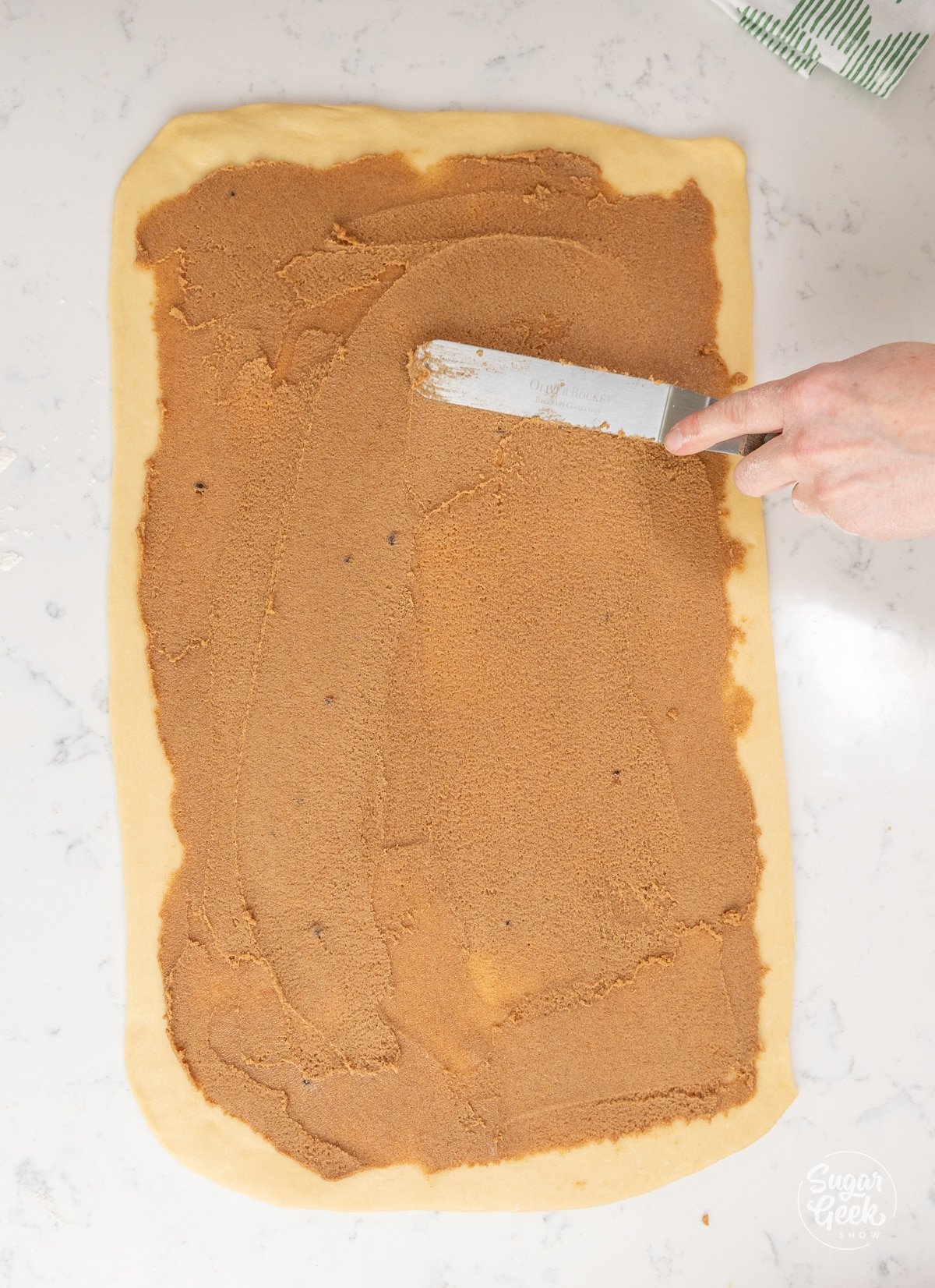 hand spreading cinnamon filling onto dough with an offset spatula