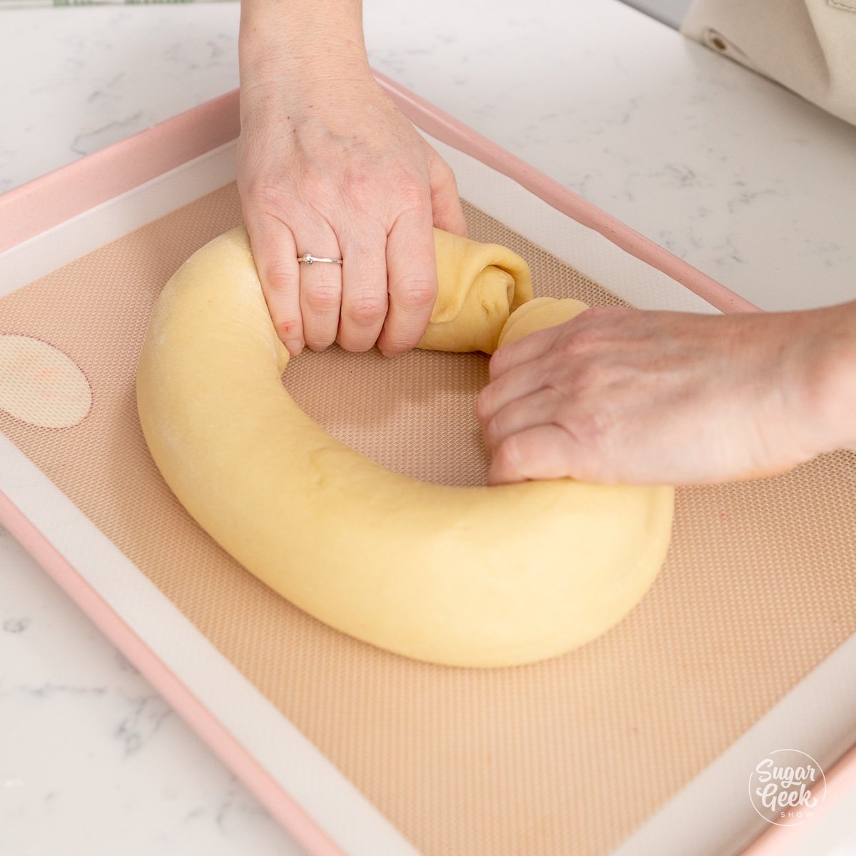 hands forming a king cake dough ring on a sheet pan