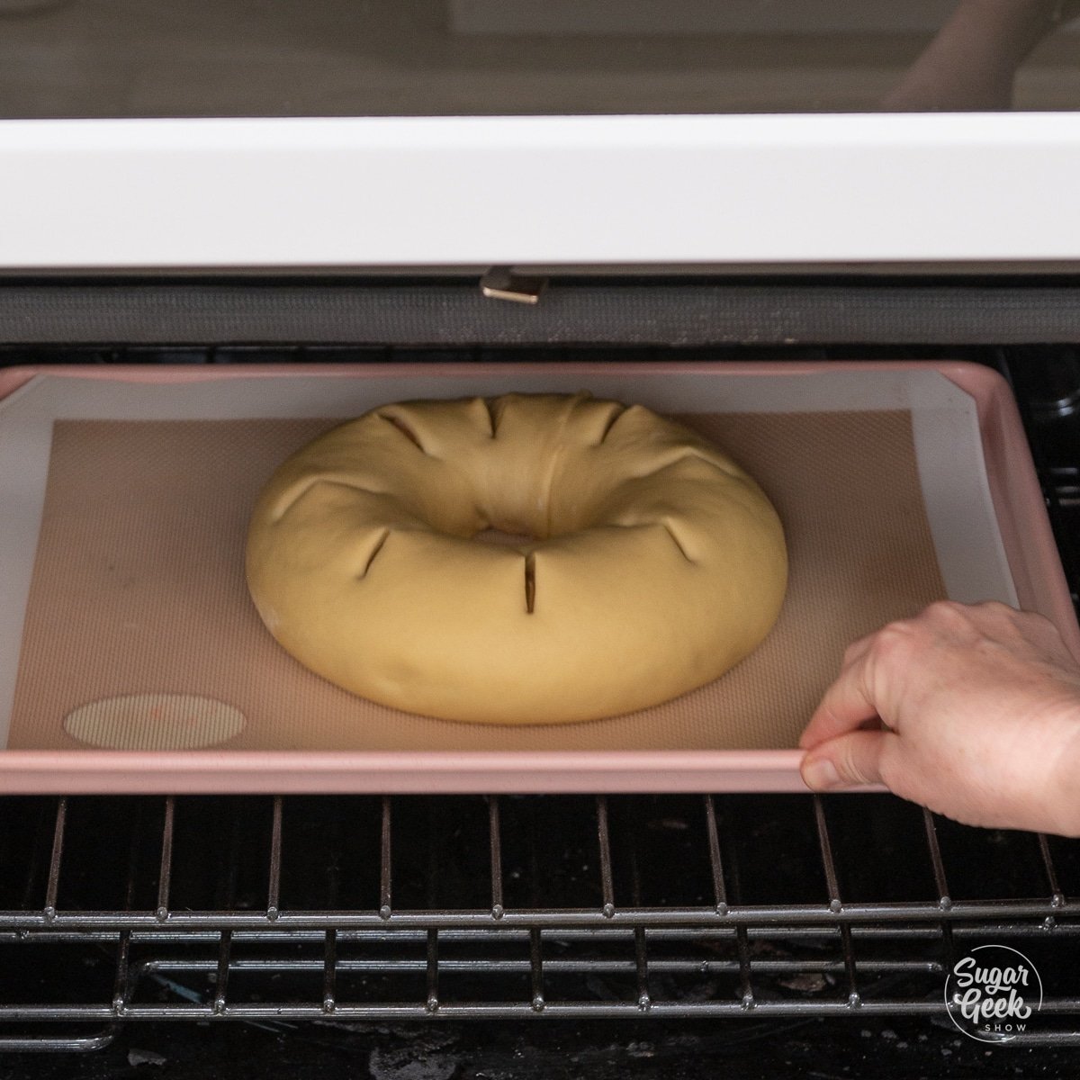hand placing a sheet pan with a king cake on it in the oven