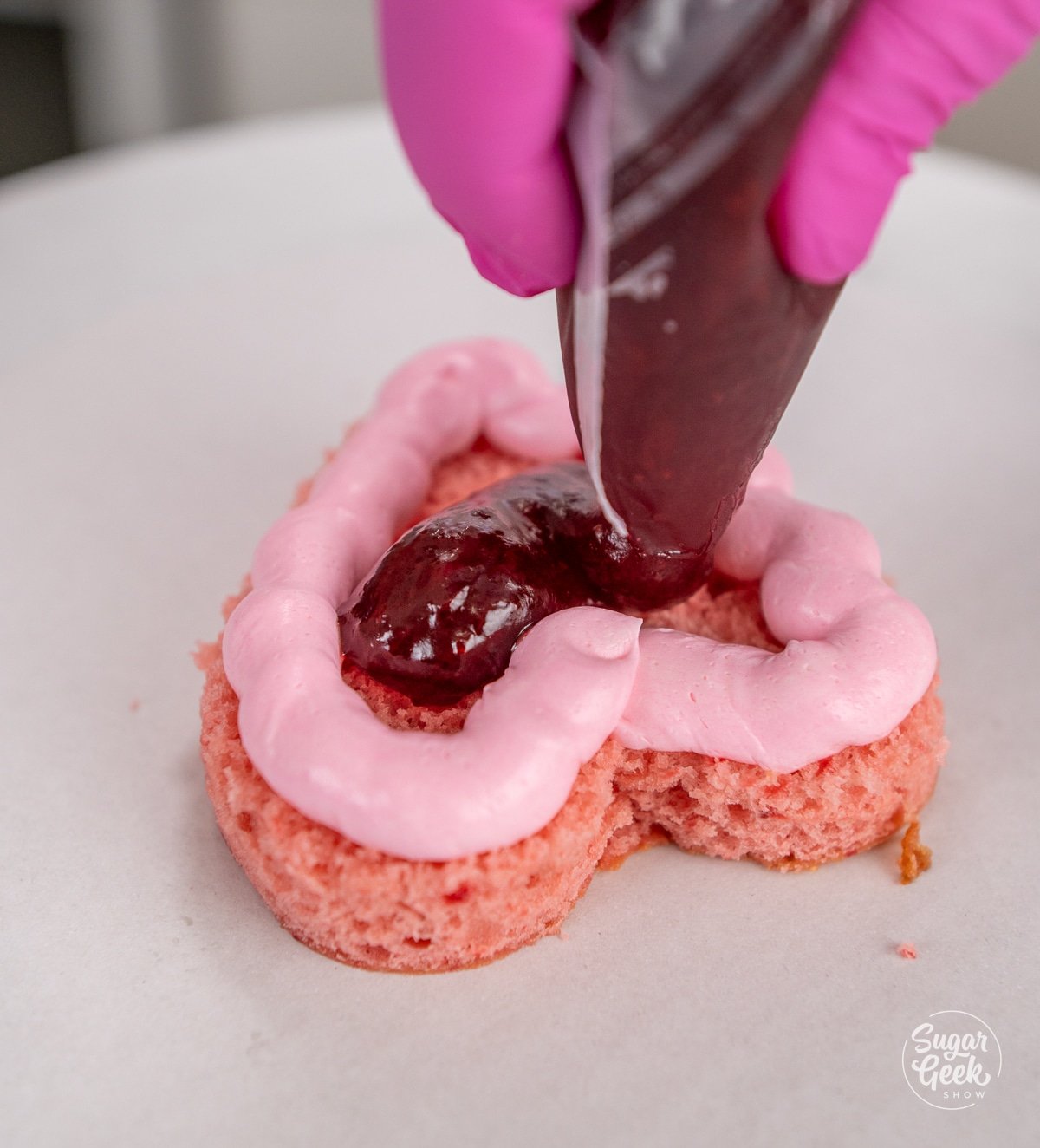 hands squeezing a piping bag of strawberry filling into a cake