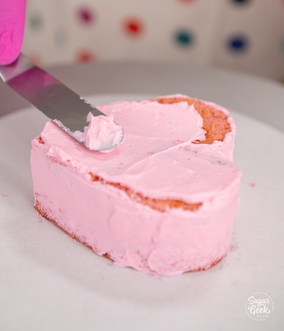 offset spatula spreading buttercream on a small heart cake